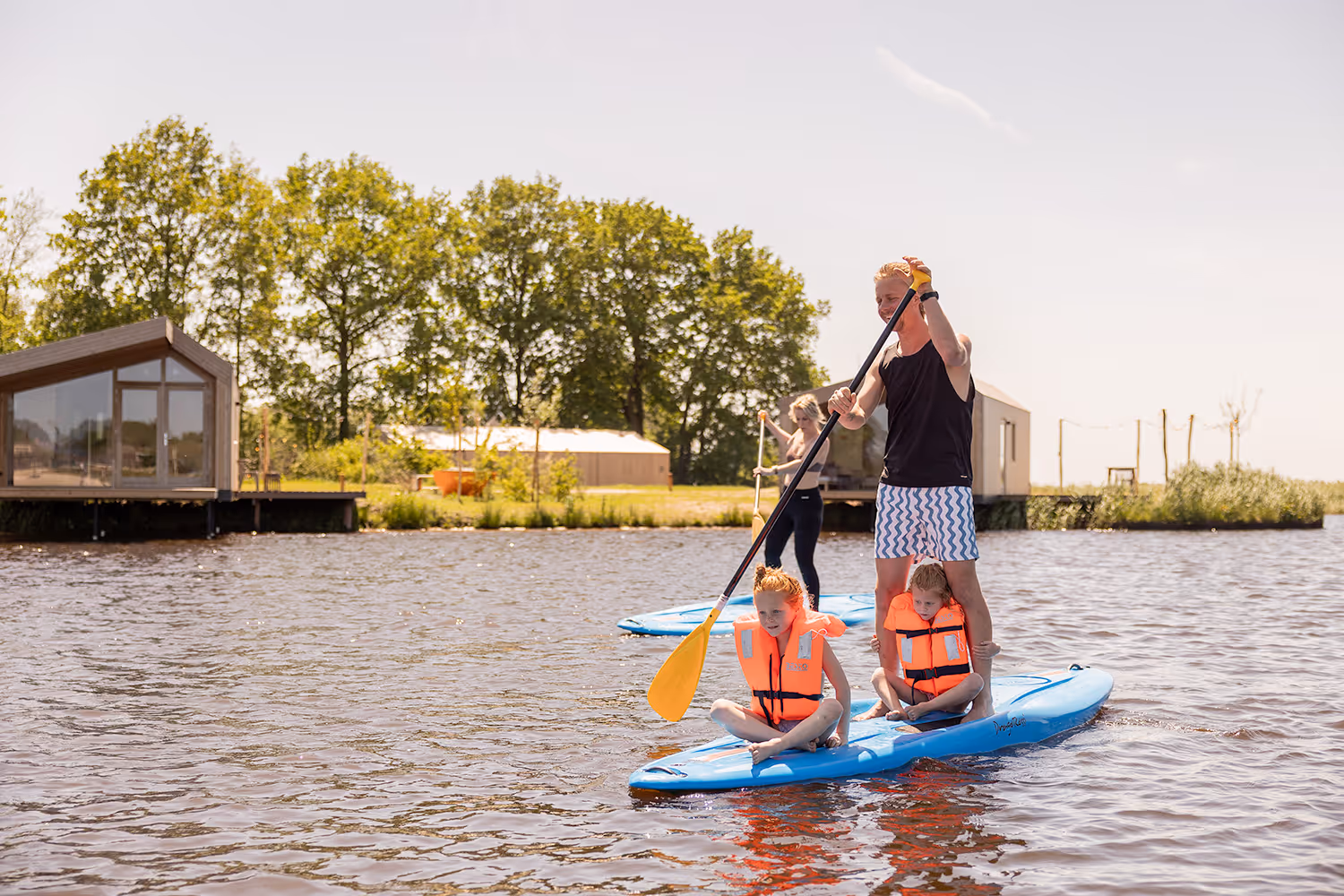 Vader peddelt op een sup met twee kinderen met zwemvesten op het water bij een waterlodge van Goudpoel in Friesland.