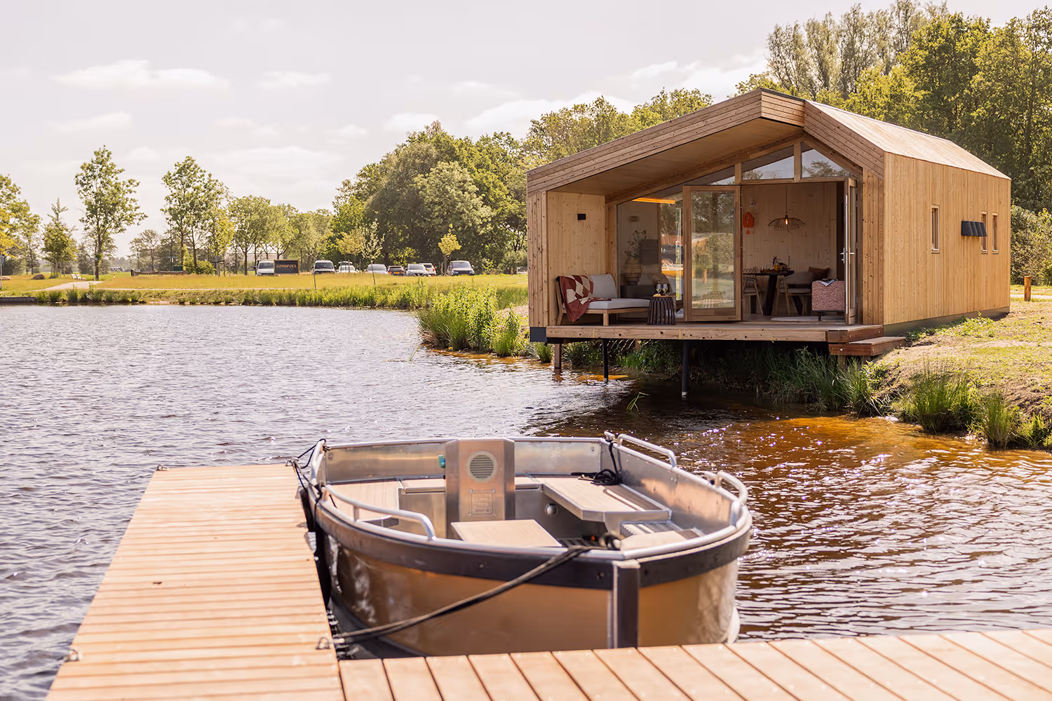 Moderne houten vakantiehuis en waterlodge met terras aan het water en een elektrische boot aangemeerd aan de steiger.