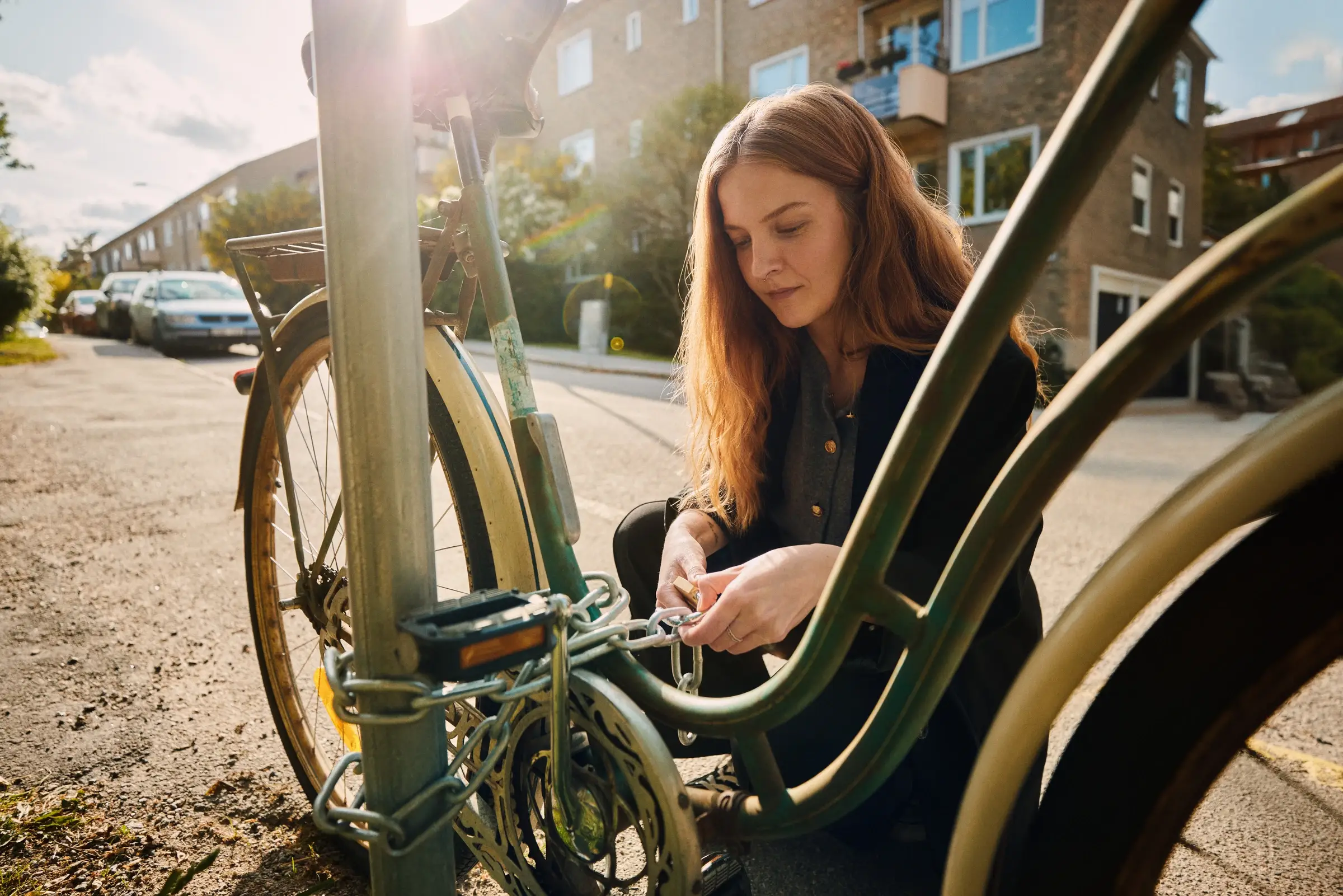 Kvinna låser fast en cykel vid en stolpe på en solig gata.