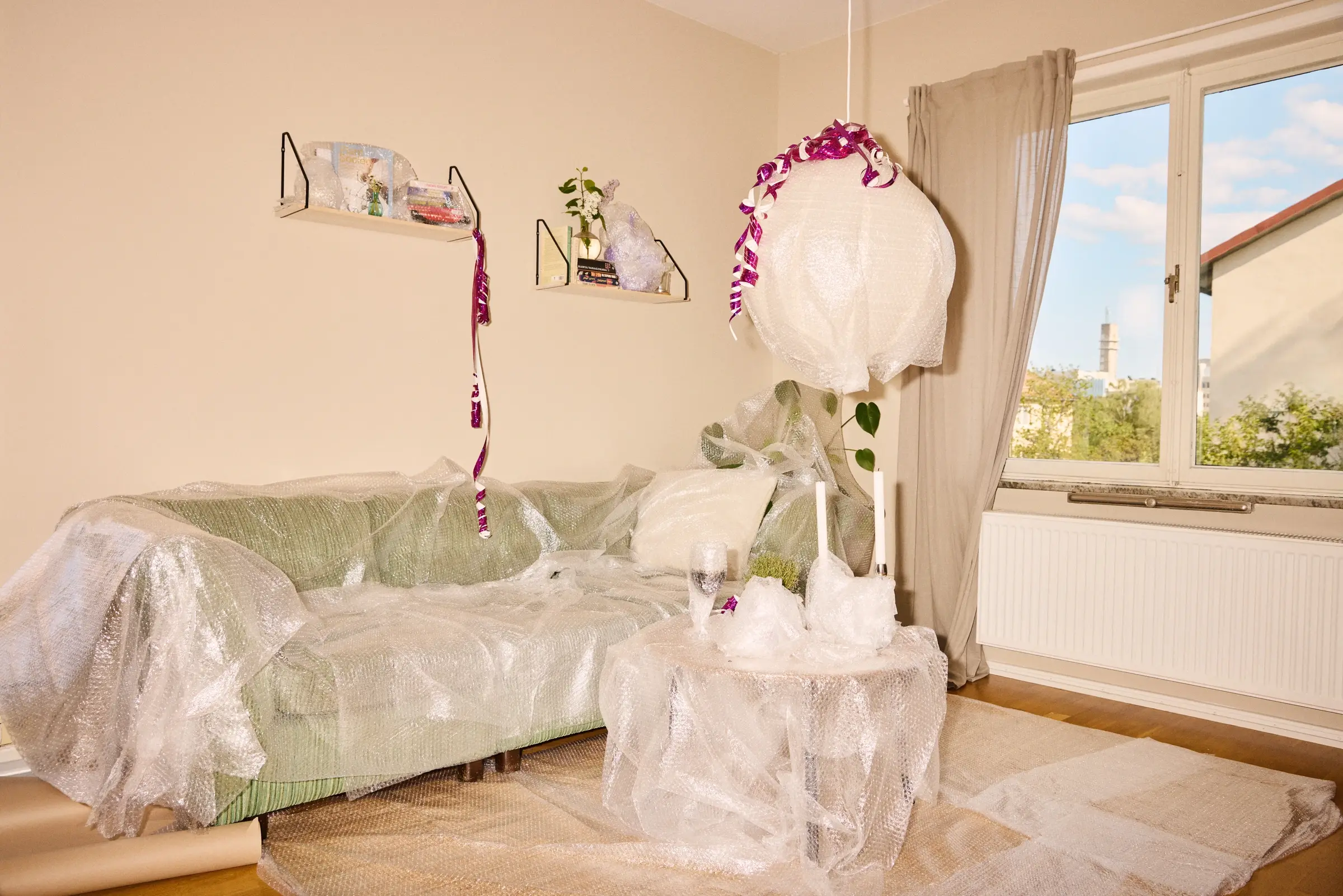 Vardagsrum med soffa, bord och lampa täckta i bubbelplast och dekorerade med serpentiner.