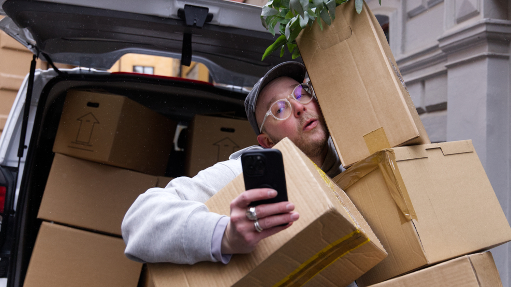 Kvinna med lockigt blont hår i grå tröja och blå byxor sitter i soffa med leopardmönstrad filt och gitarr bredvid.