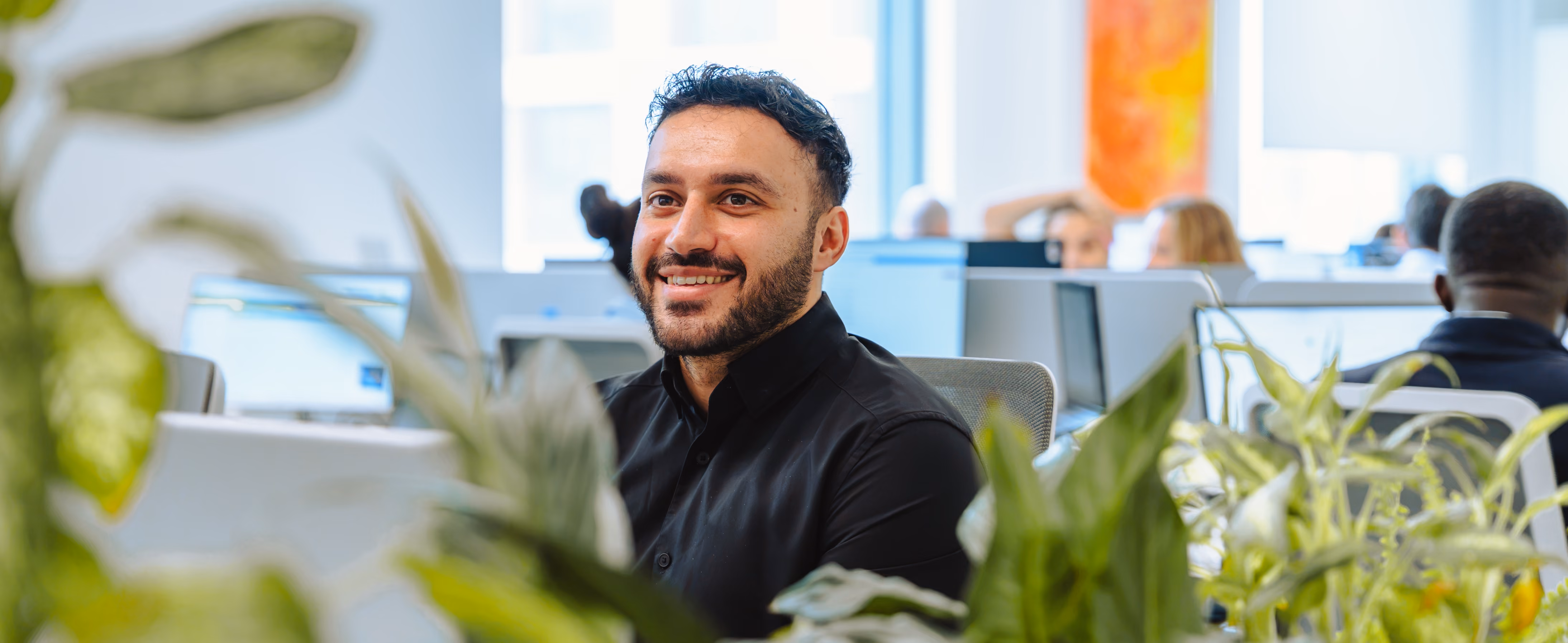 Professional man smiling in modern office with plants and colleagues working in background