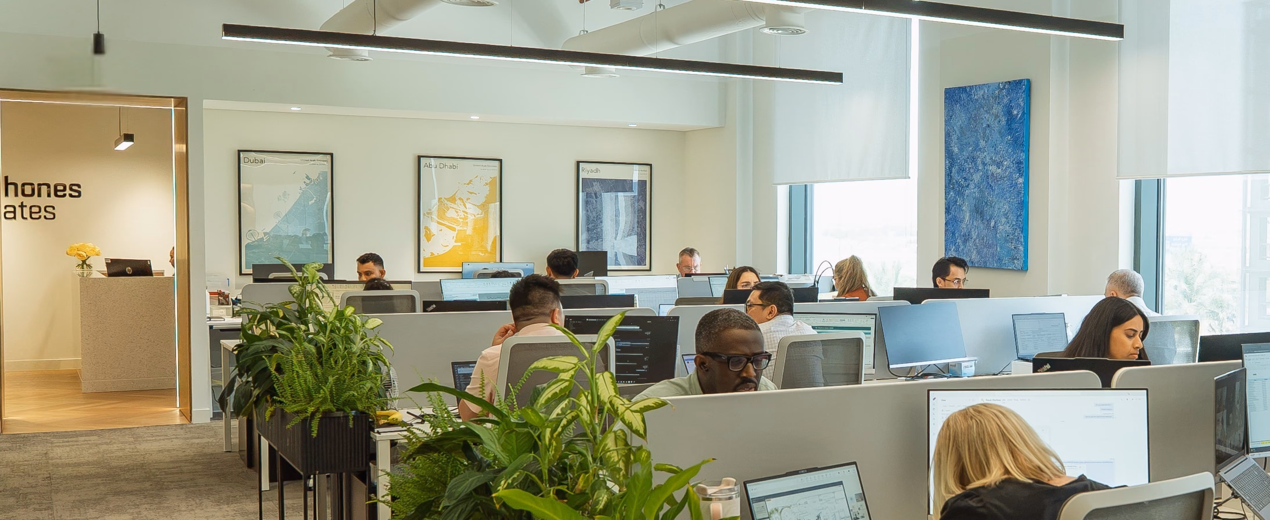 Modern office space with diverse employees working at desks with computers and plants.