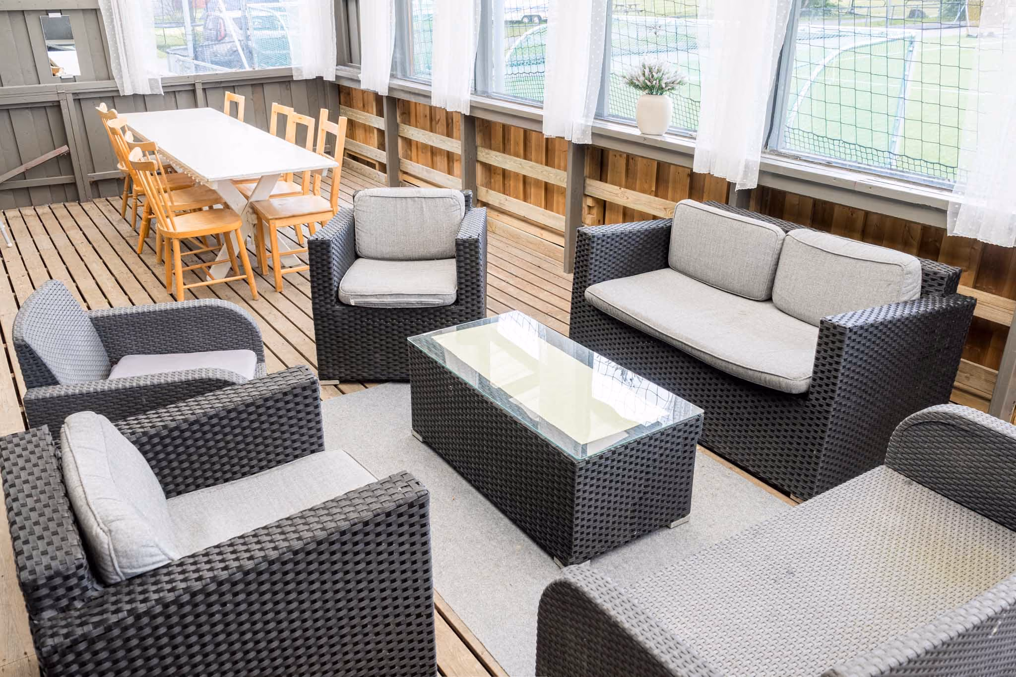 Utemøbler av kurv med pute rundt et glassbord ved siden av et bord med seks trestoler på en terrasse.