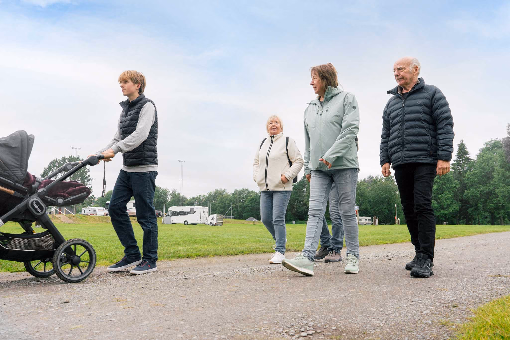 Ung gutt skyver barnevogn i parkeringsområde med tre eldre voksne som går ved siden av ham.