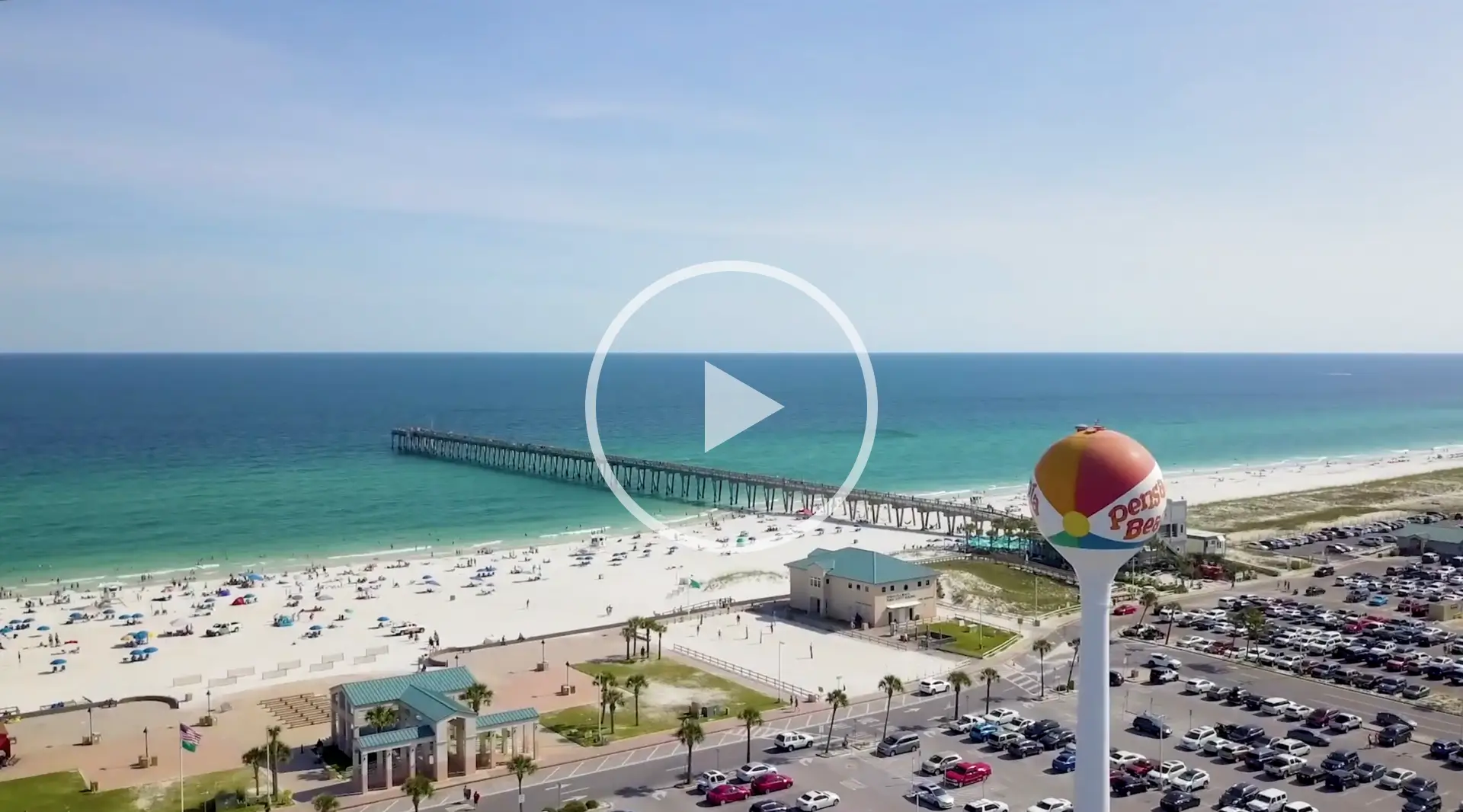 Arial view of a beach with a pier, sandy shore, and a colorful water tower.