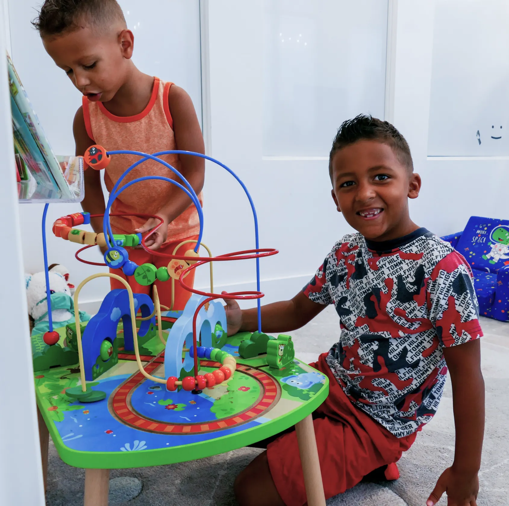 Two children playing with a colorful bead maze toy on a small table.