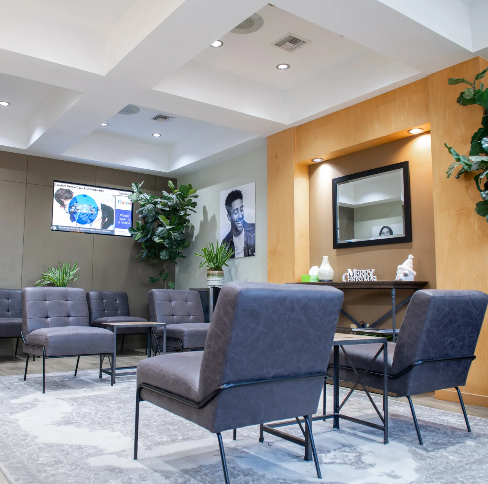 A waiting area with grey chairs, a rug, plants, and a mirror on the wall.