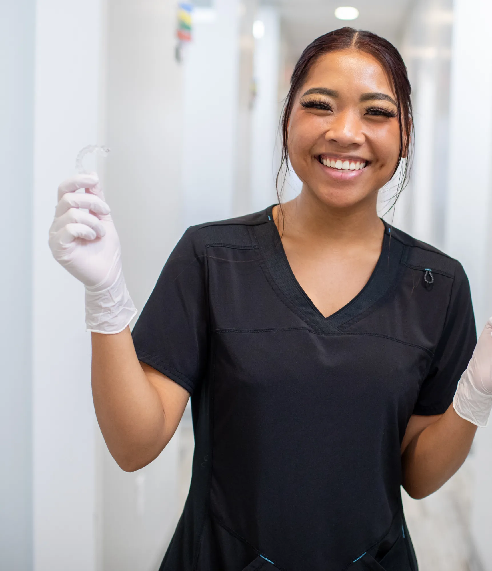 Smiling dental assistant holding a dental mold in a clinic hallway.
