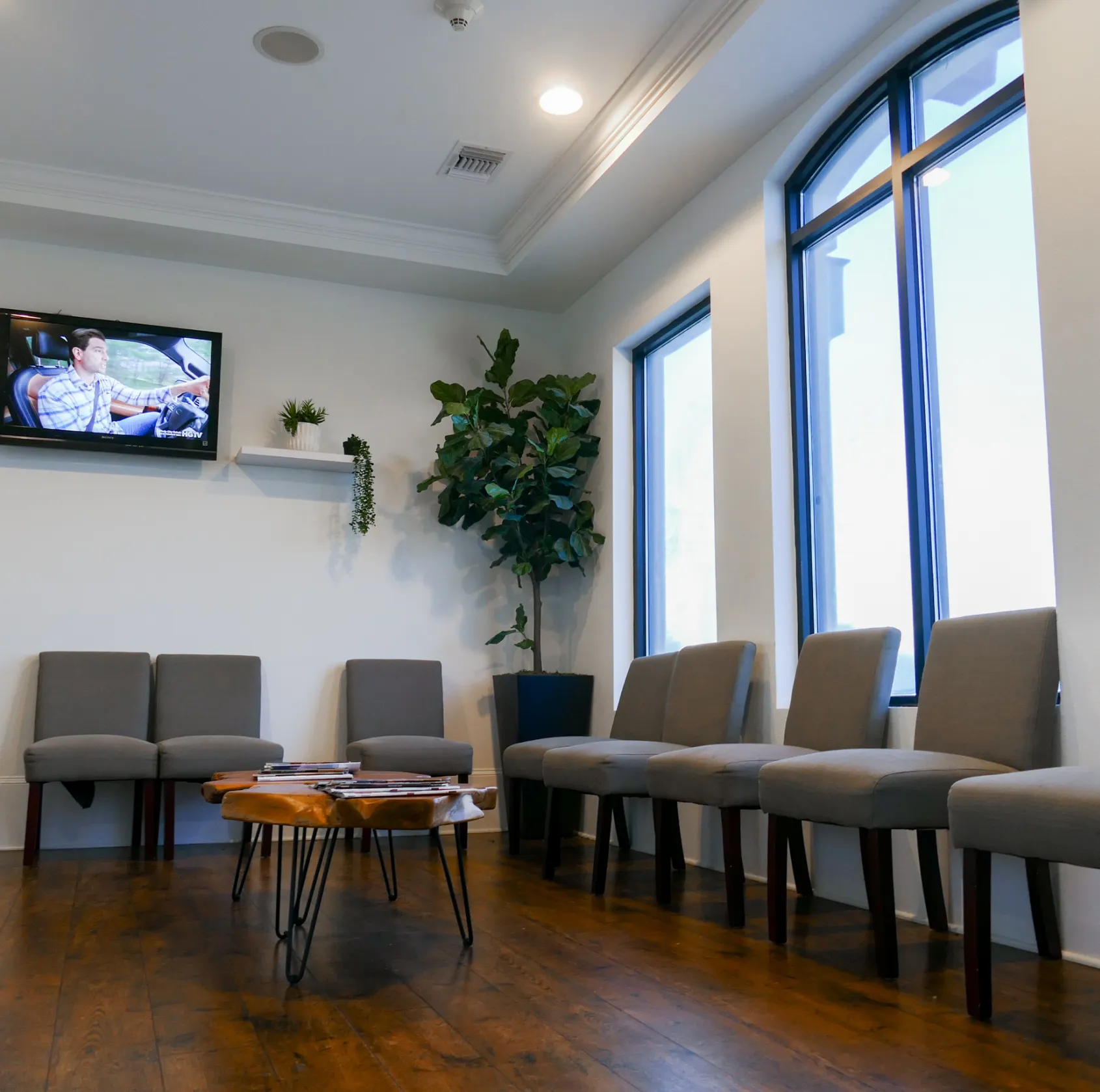Empty waiting room with gray chairs and a TV showing a person driving.