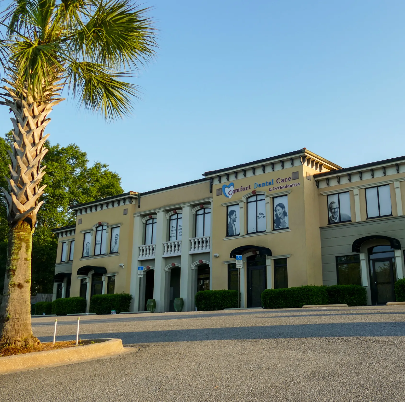 A woman sitting in a dentist's chair is placing a clear dental aligner in her mouth.