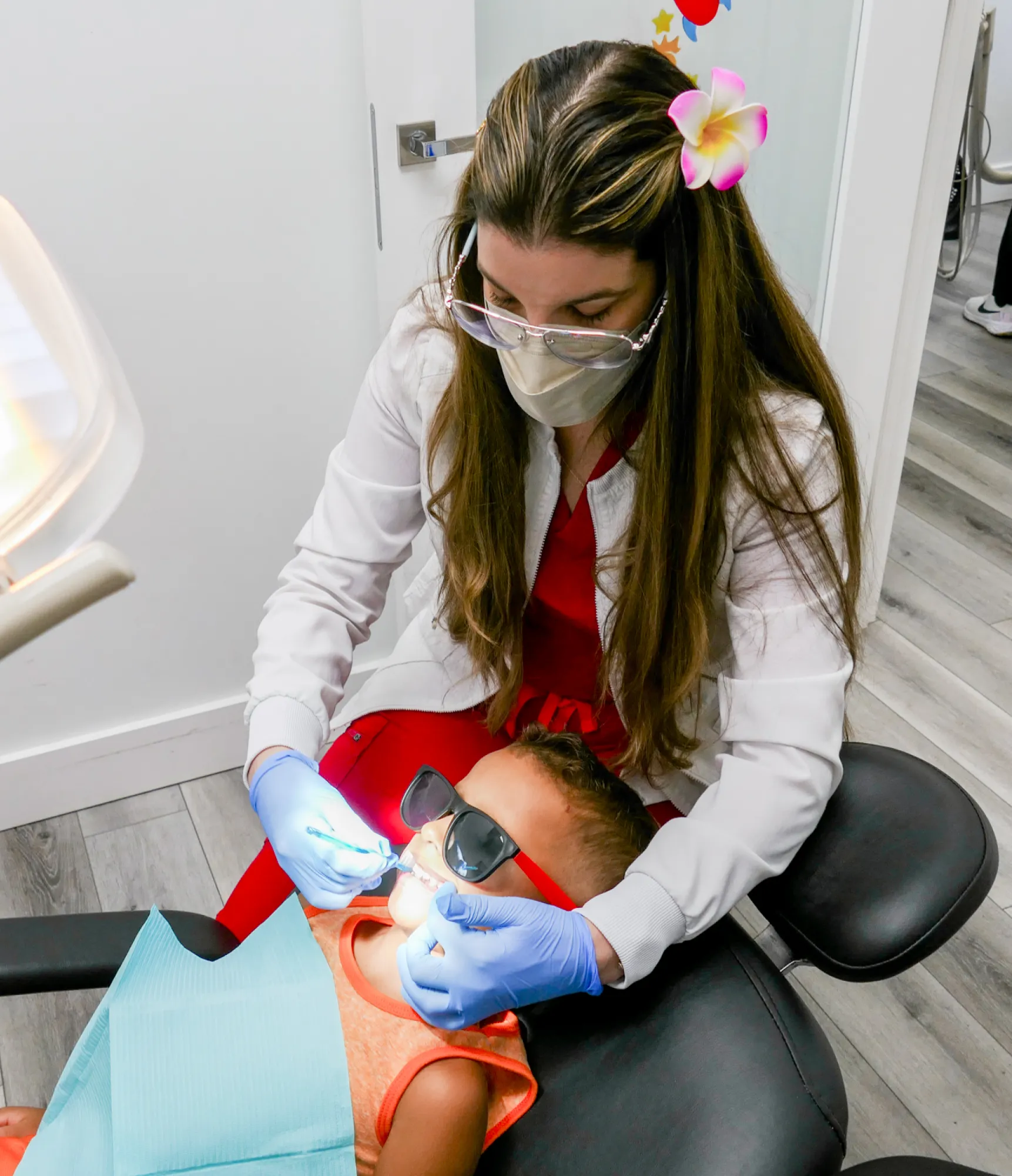 A bright waiting room with white chairs lined up against a wall under three large windows.