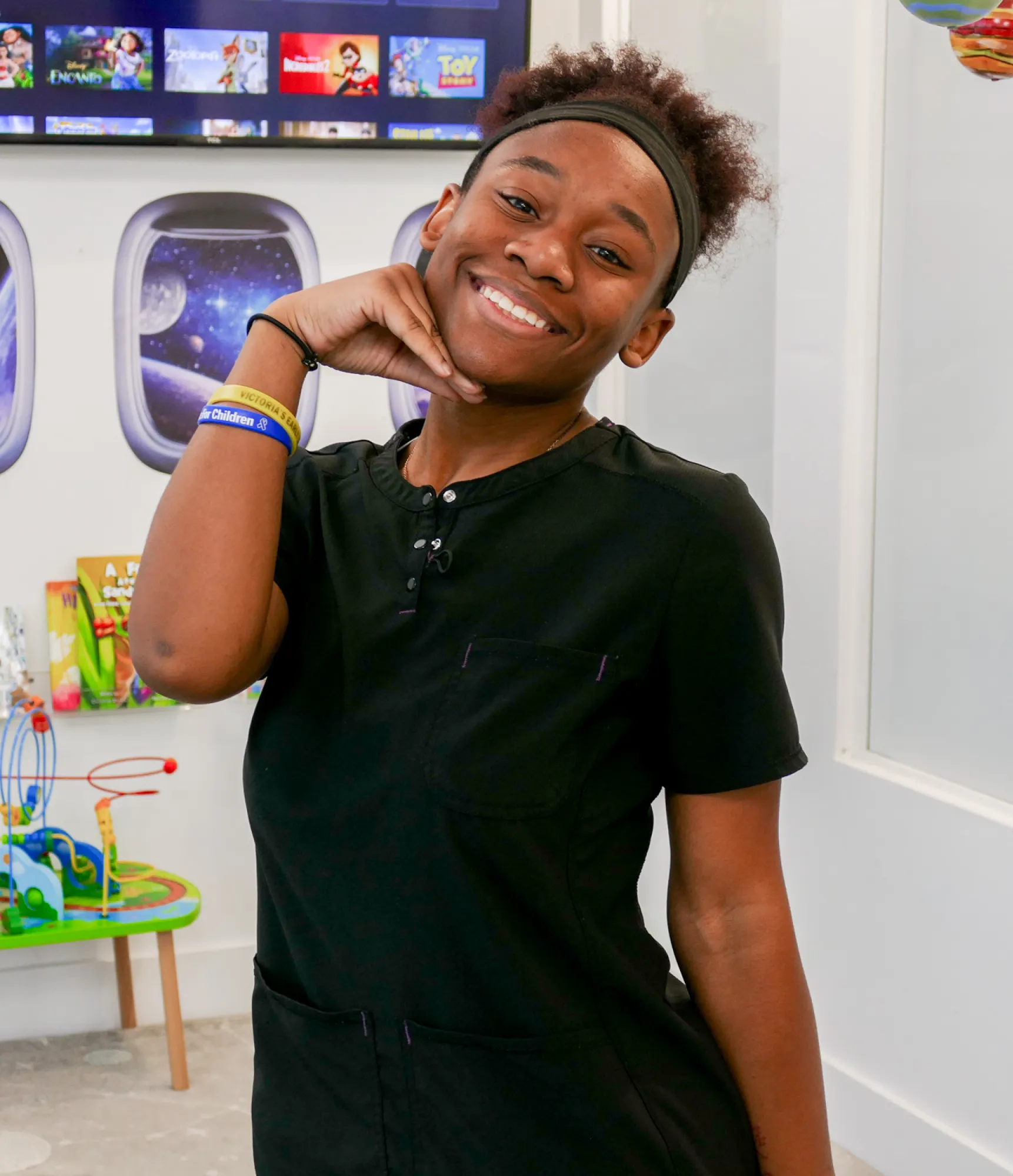 A person in black clothing is smiling and posing with one hand under their chin.