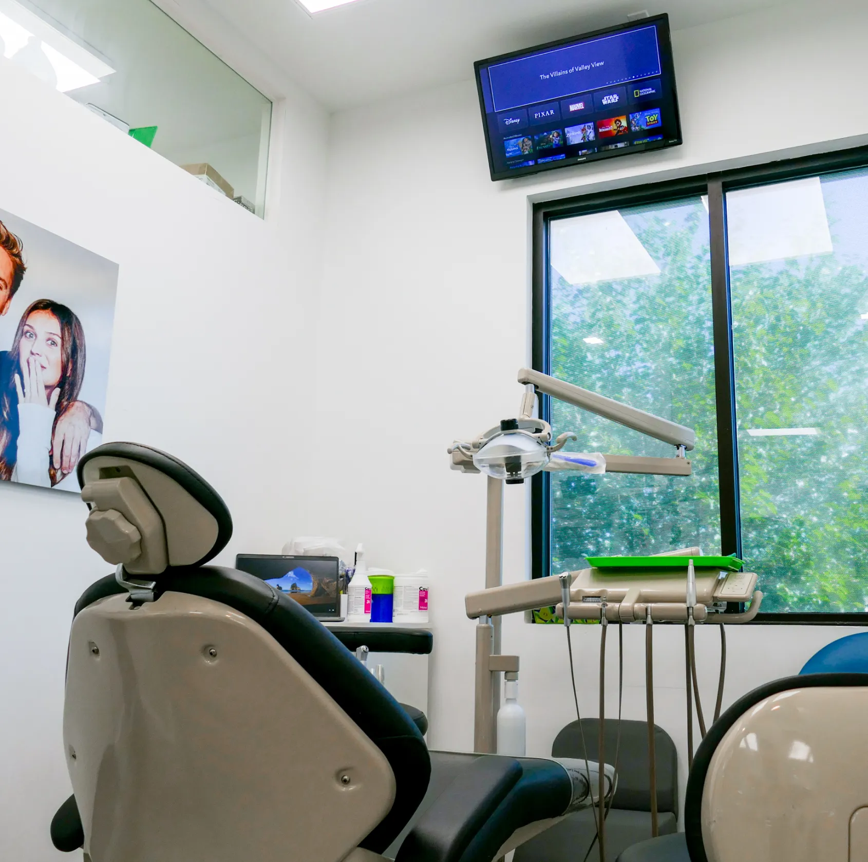 Dental office with an empty exam chair and dental equipment, television on the wall above.