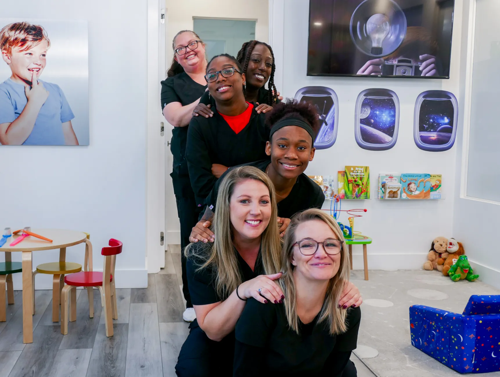 Three women standing and smiling, embracing each other in an office setting.