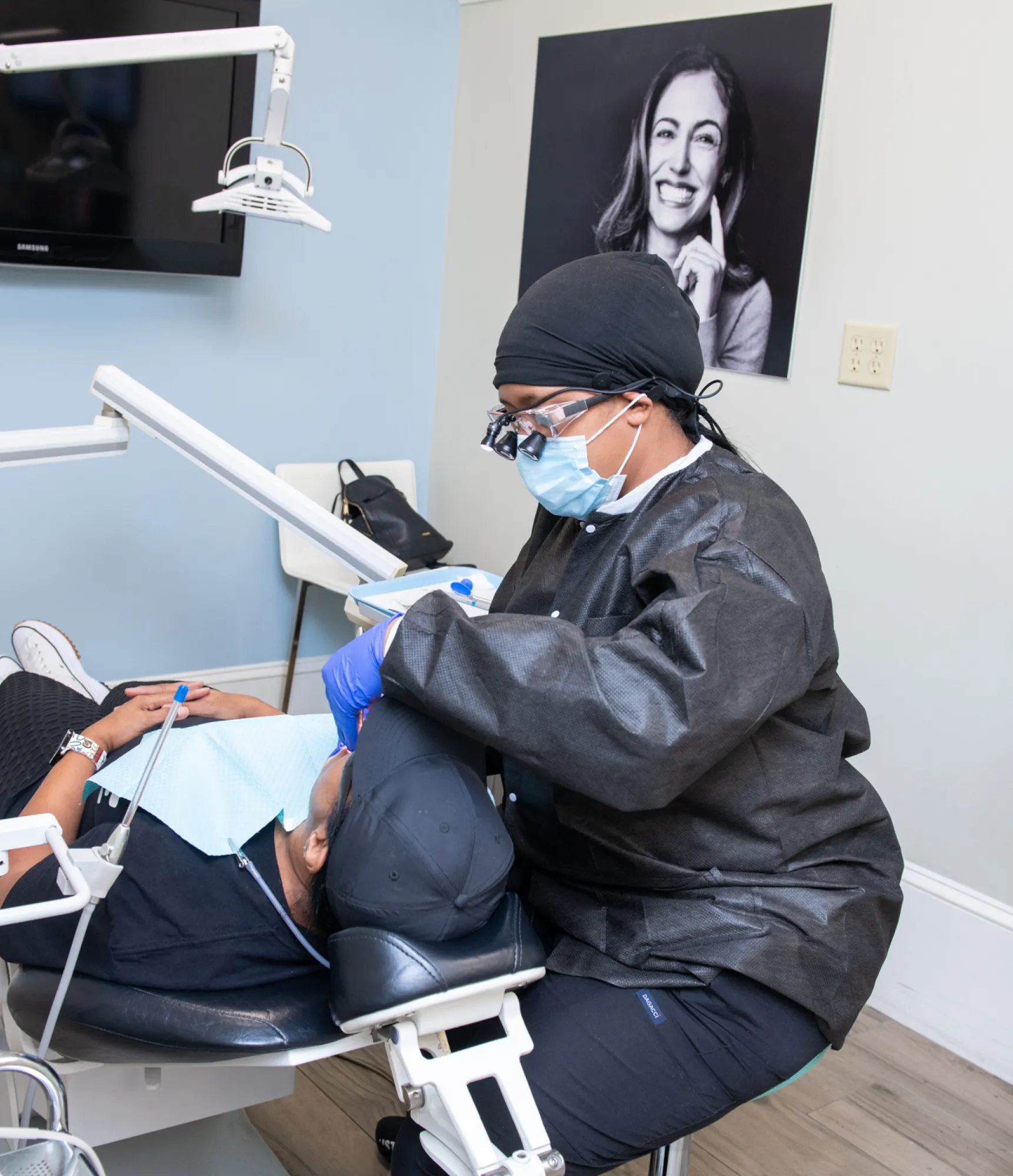 Dentist wearing protective gear examines a patient lying in a dental chair.