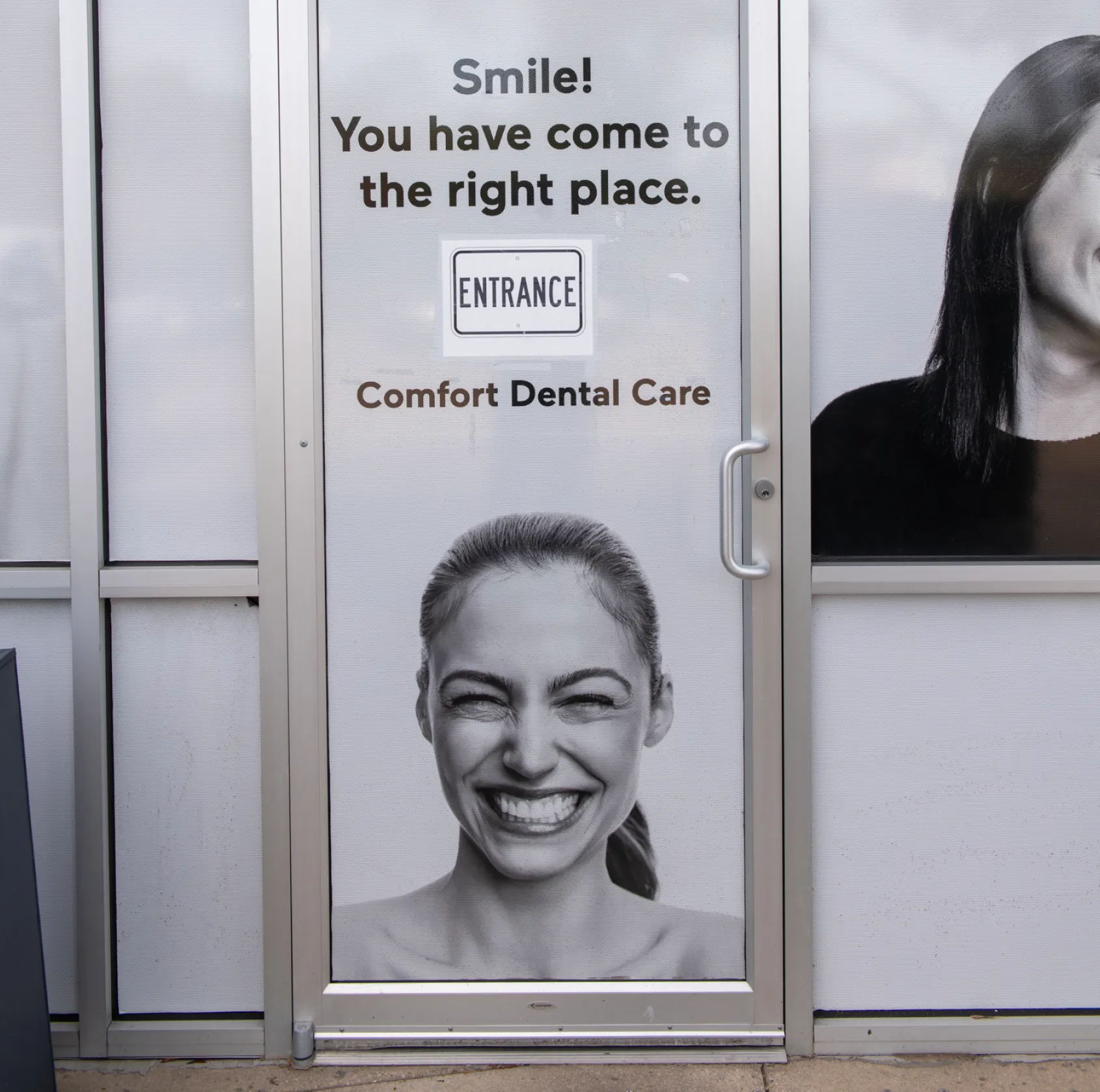 A woman with glasses smiles in a dental office, standing near dental equipment.