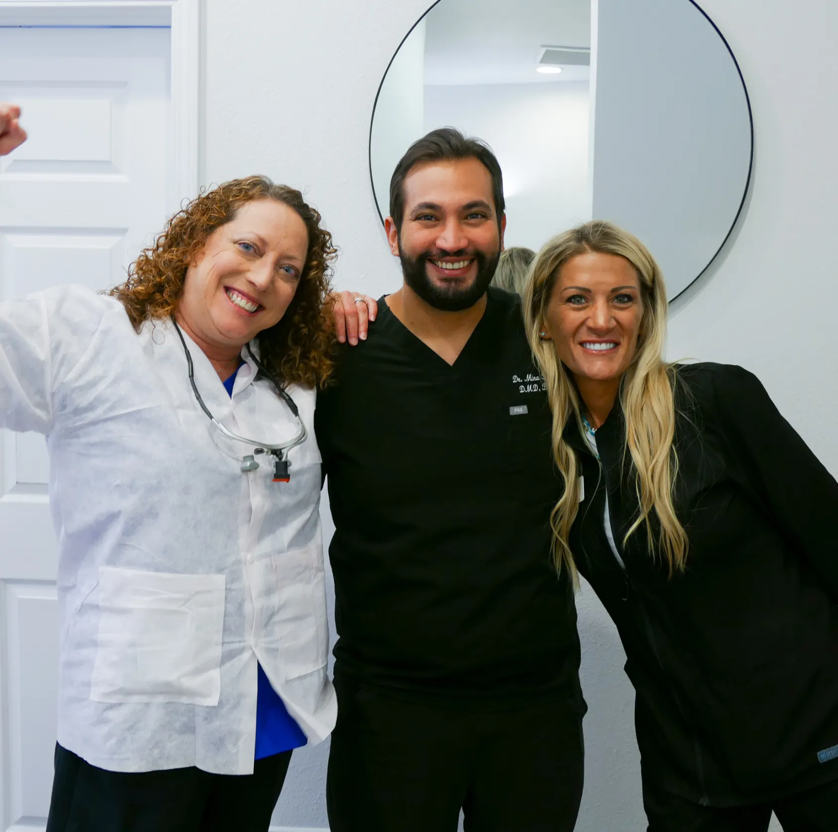 Man in black scrubs gives a thumbs-up while standing in an office near a printer.
