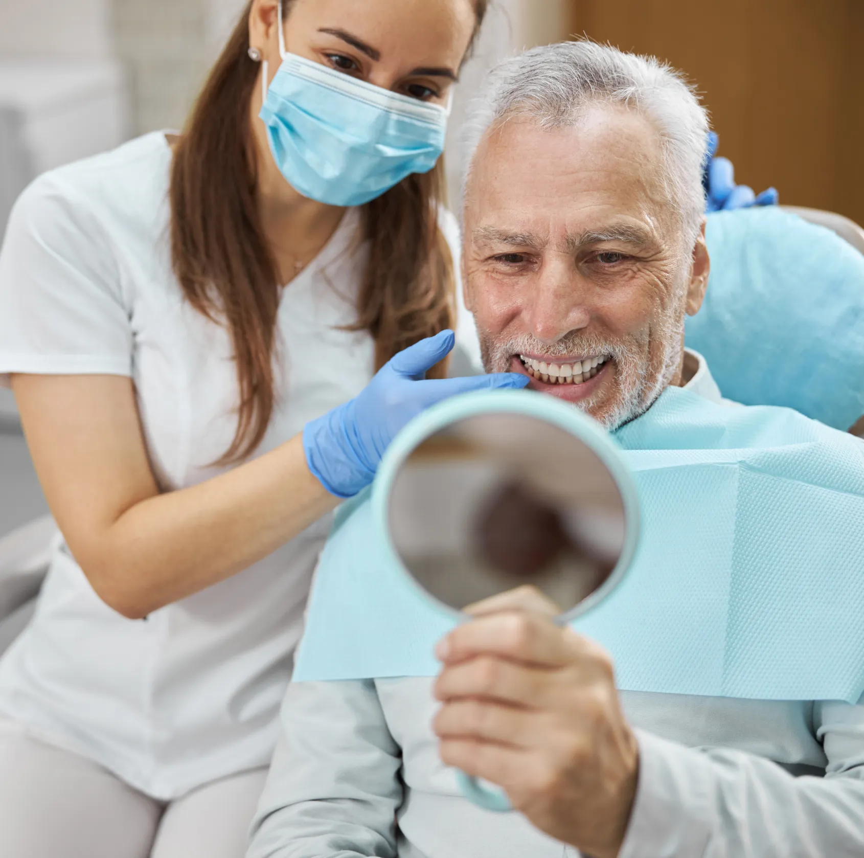 A dentist wearing gloves demonstrates a dental implant to a patient.