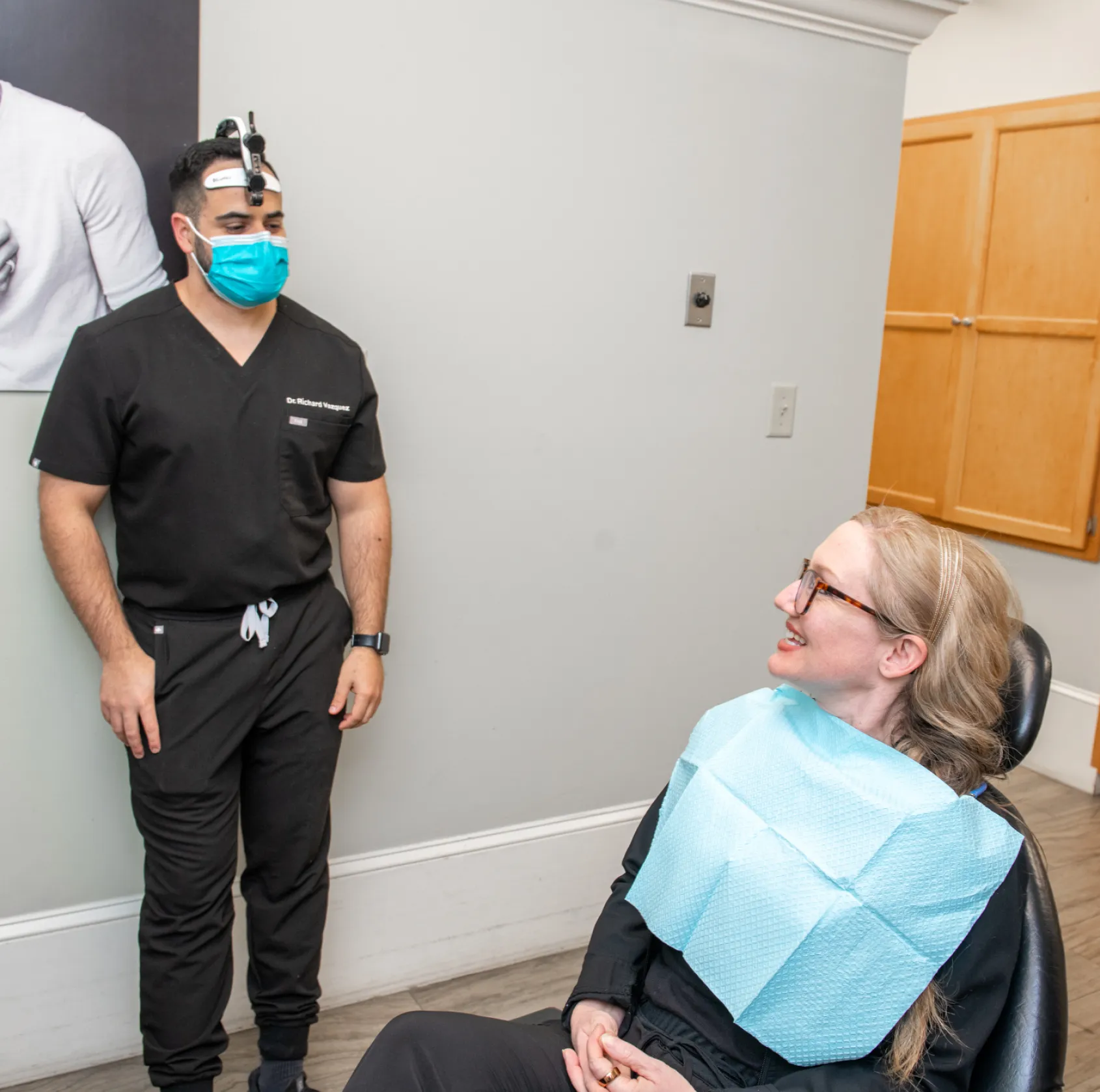 Two women in an office; one smiles at the camera, the other works on a computer.