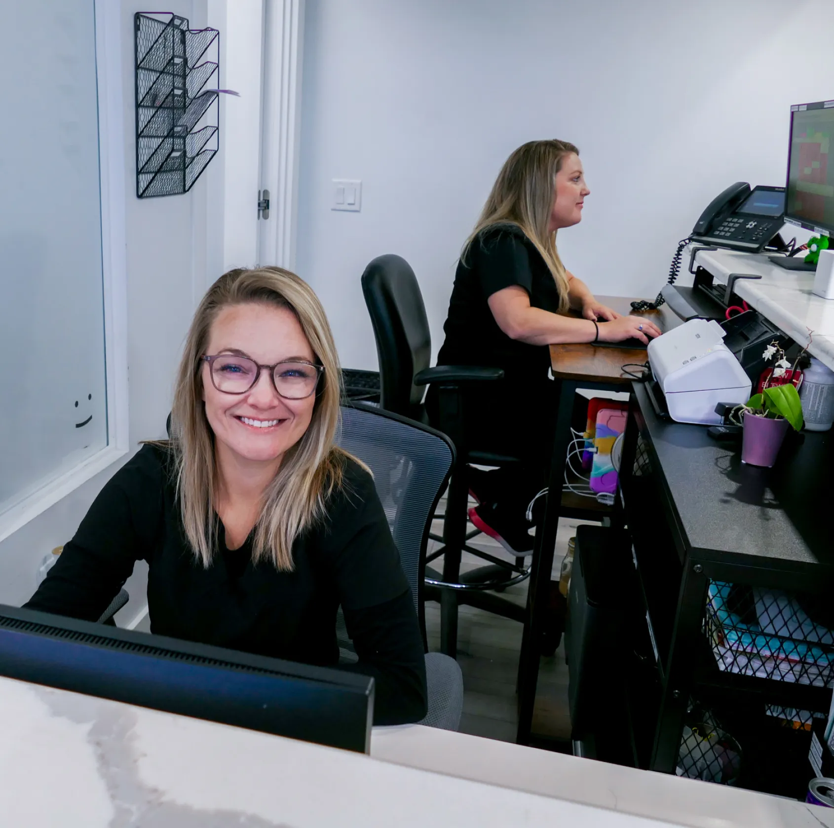 A dental hygienist cleans a young boy's teeth while another child watches and smiles.