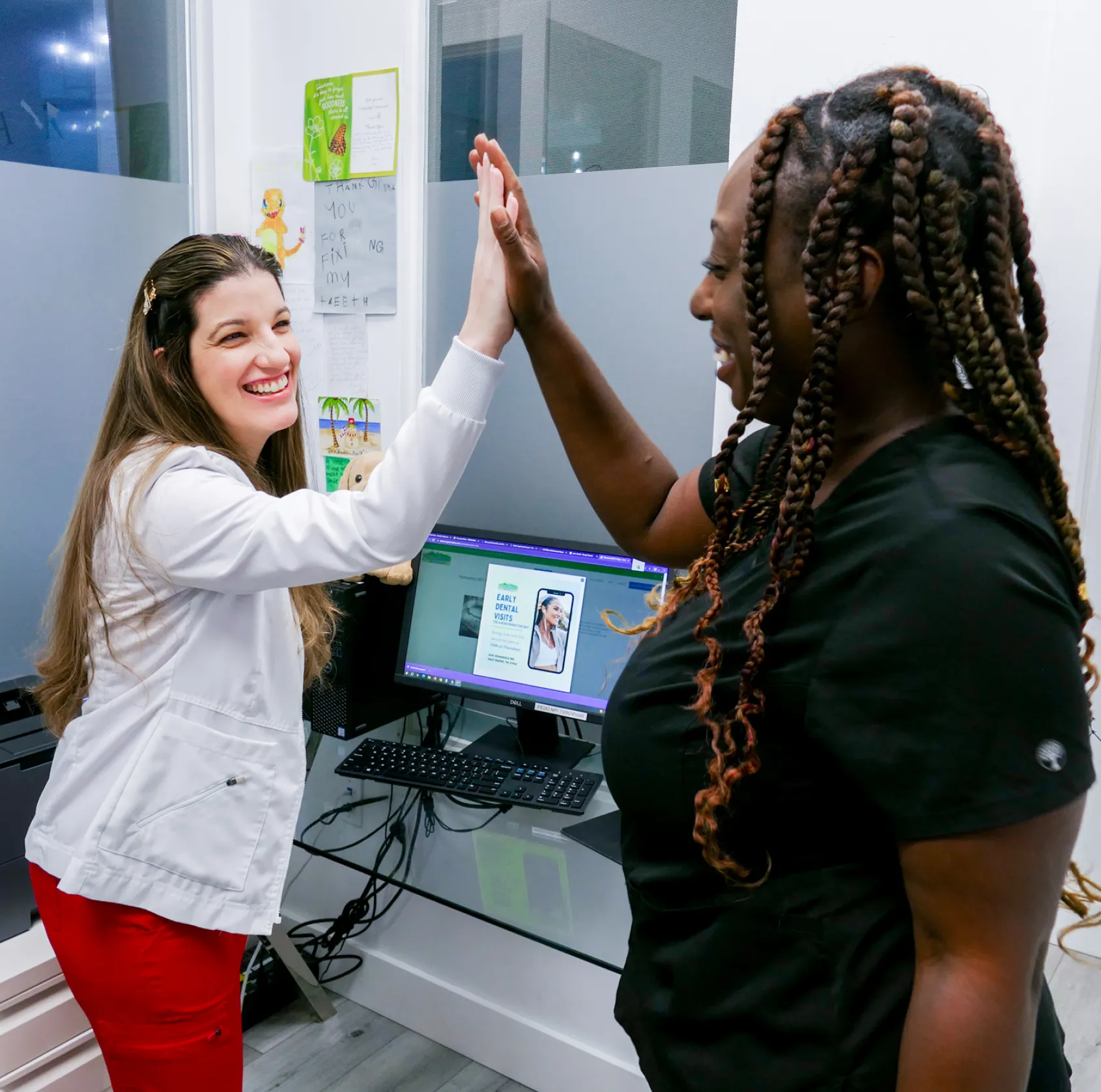 A woman sits in a dental chair, smiling and listening to a dental professional talking.