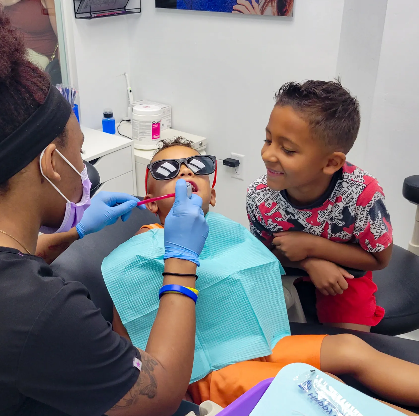 Person holding a mirror, reflecting their smiling face with dental equipment in the background.