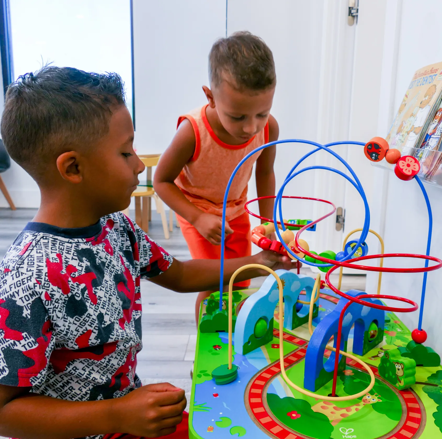 A man with glasses and a patterned shirt smiles while crossing his arms indoors.