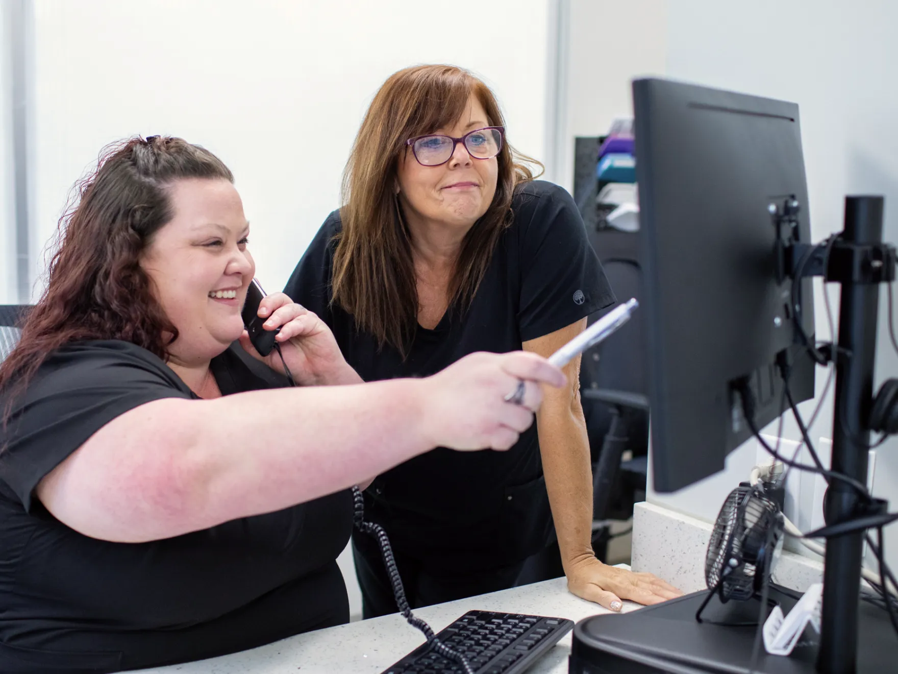 Three women collaborating while looking at a laptop screen in a professional setting.