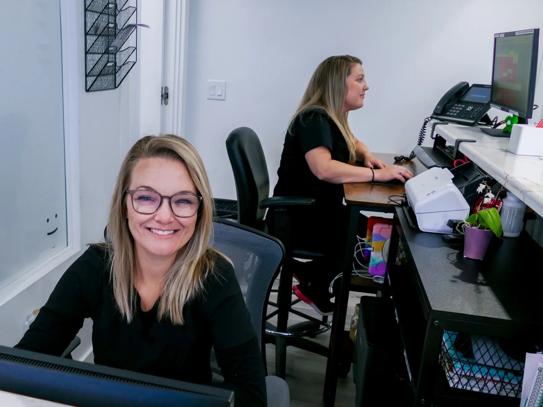 A woman sitting on the floor smiles while talking on the phone and using a laptop.