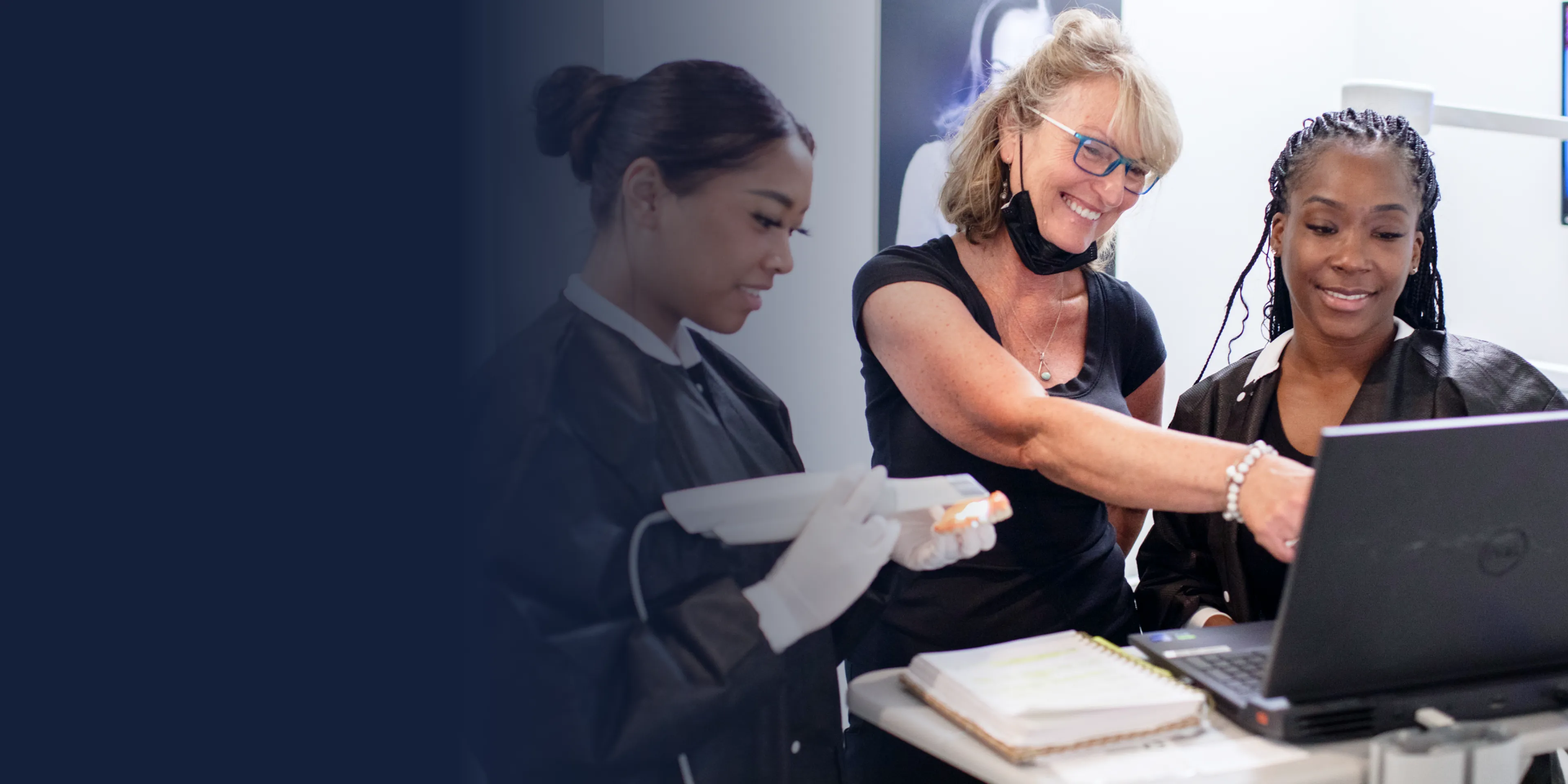Three people are collaborating around a laptop, with one person pointing at the screen.