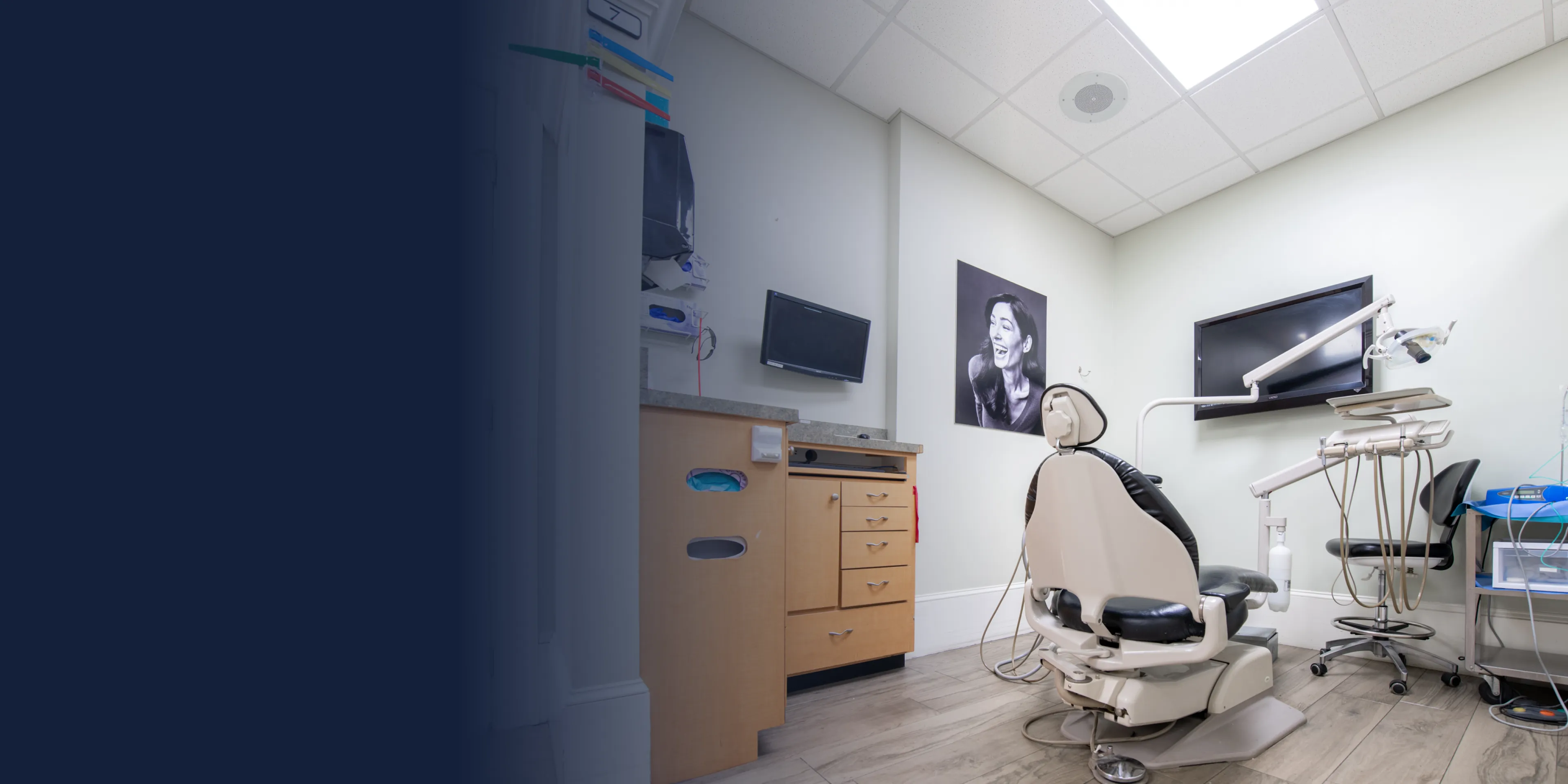 A dentist's office with a dental chair, overhead light, and TV screen on the wall.