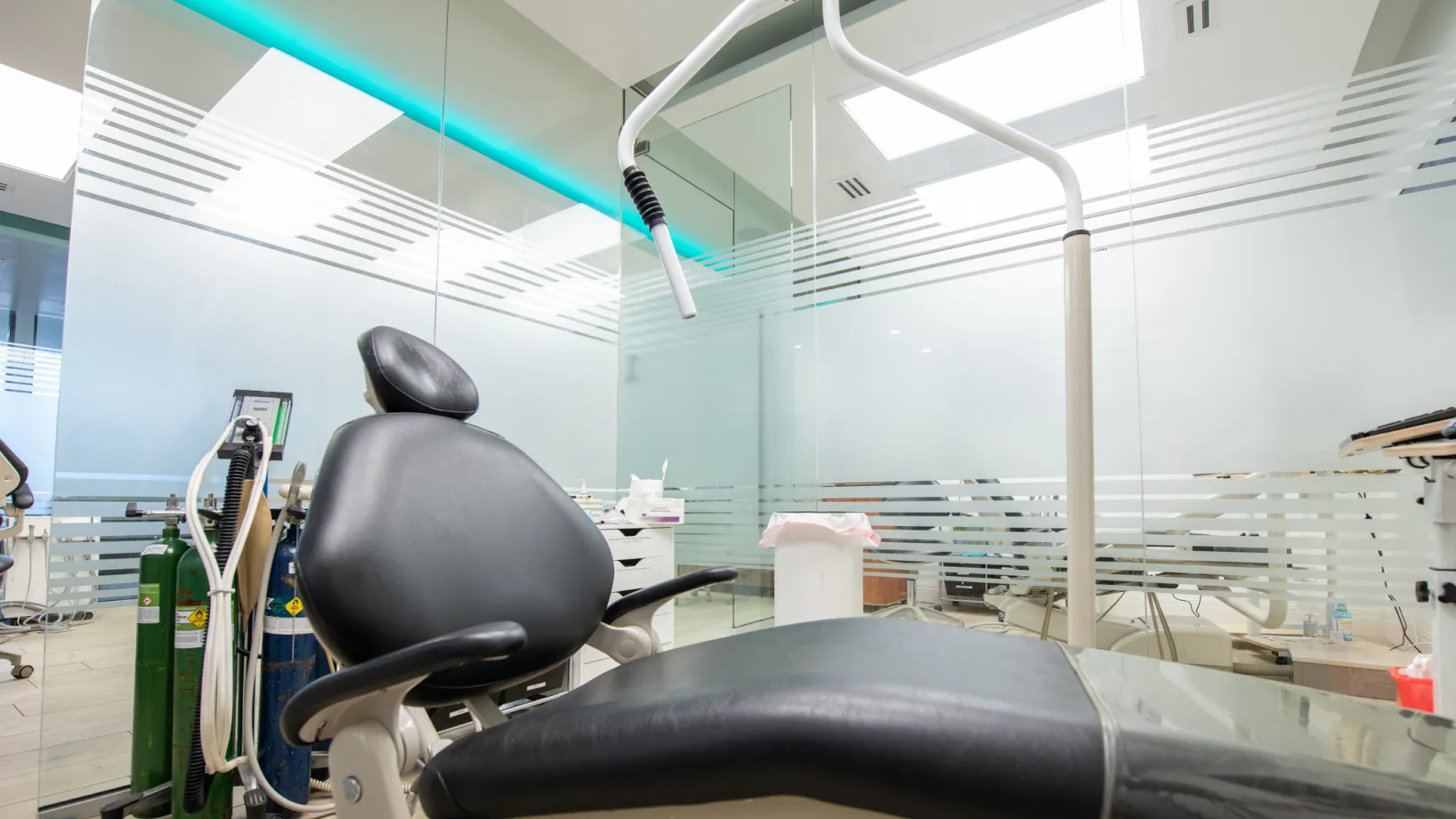 A waiting room with gray chairs, a TV on the wall, and plants in the corners.