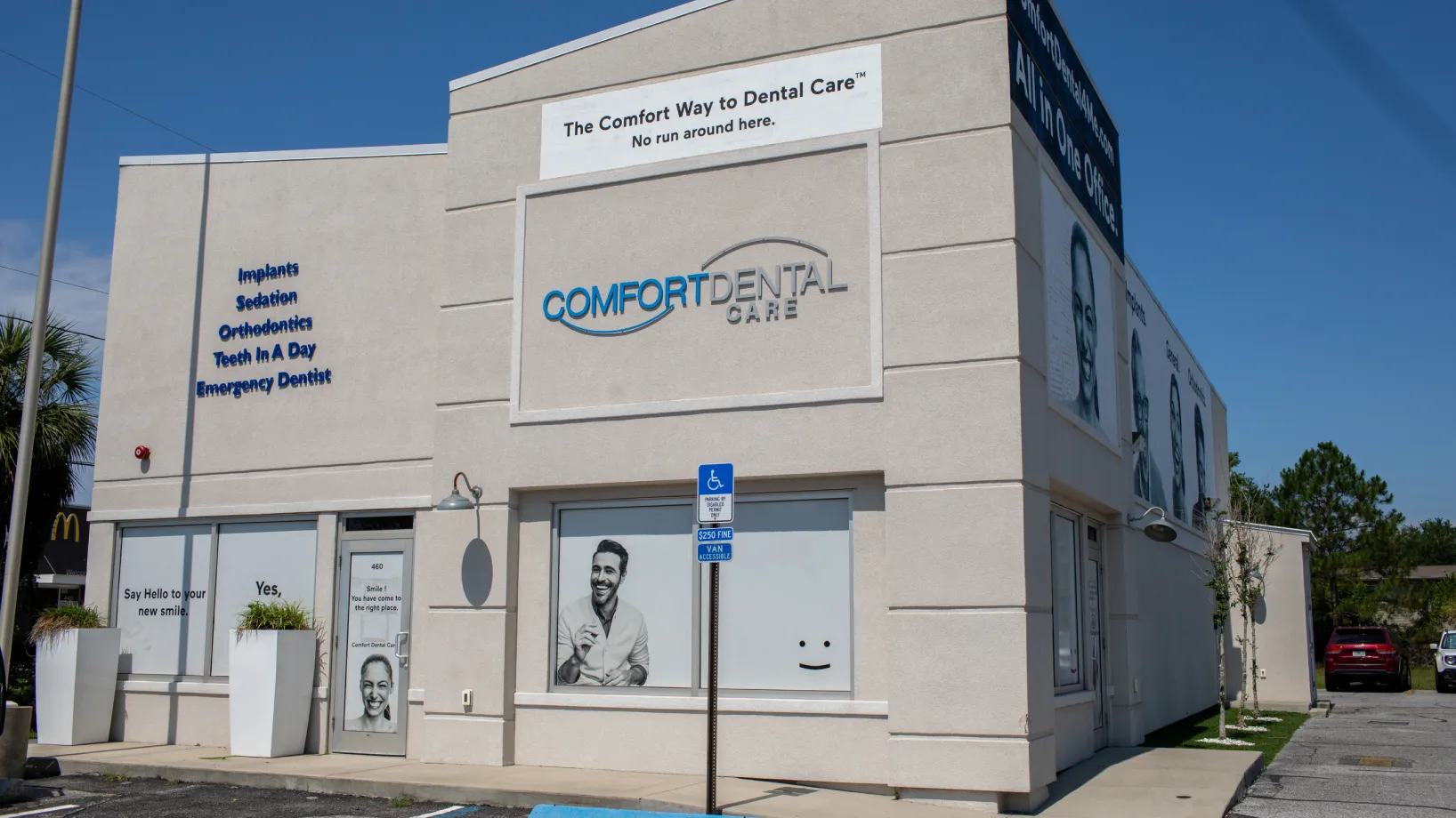 A waiting room with empty black chairs, a gray couch, plants, and a small wooden table.