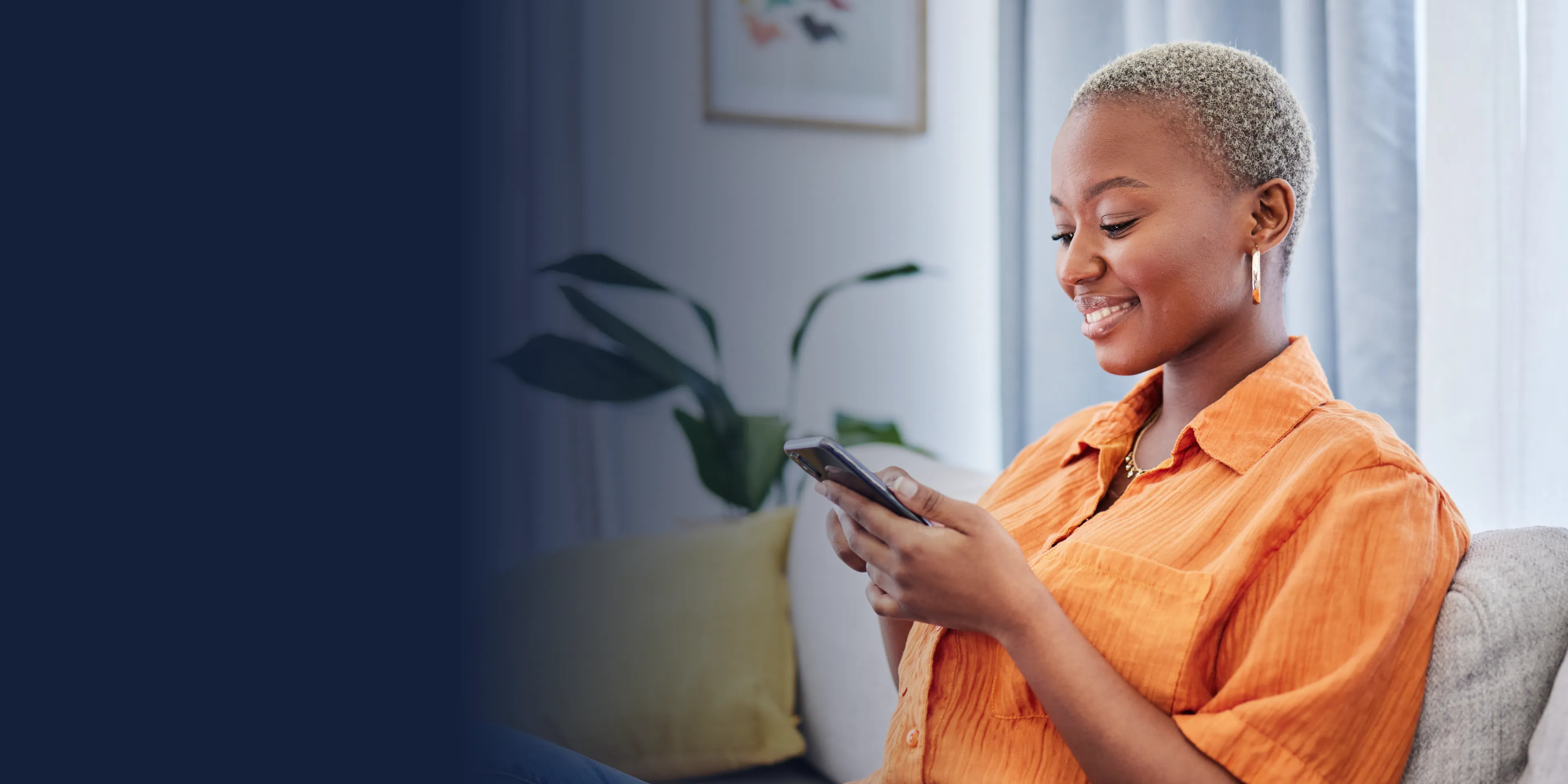 A woman in an orange shirt smiles while looking at her phone.