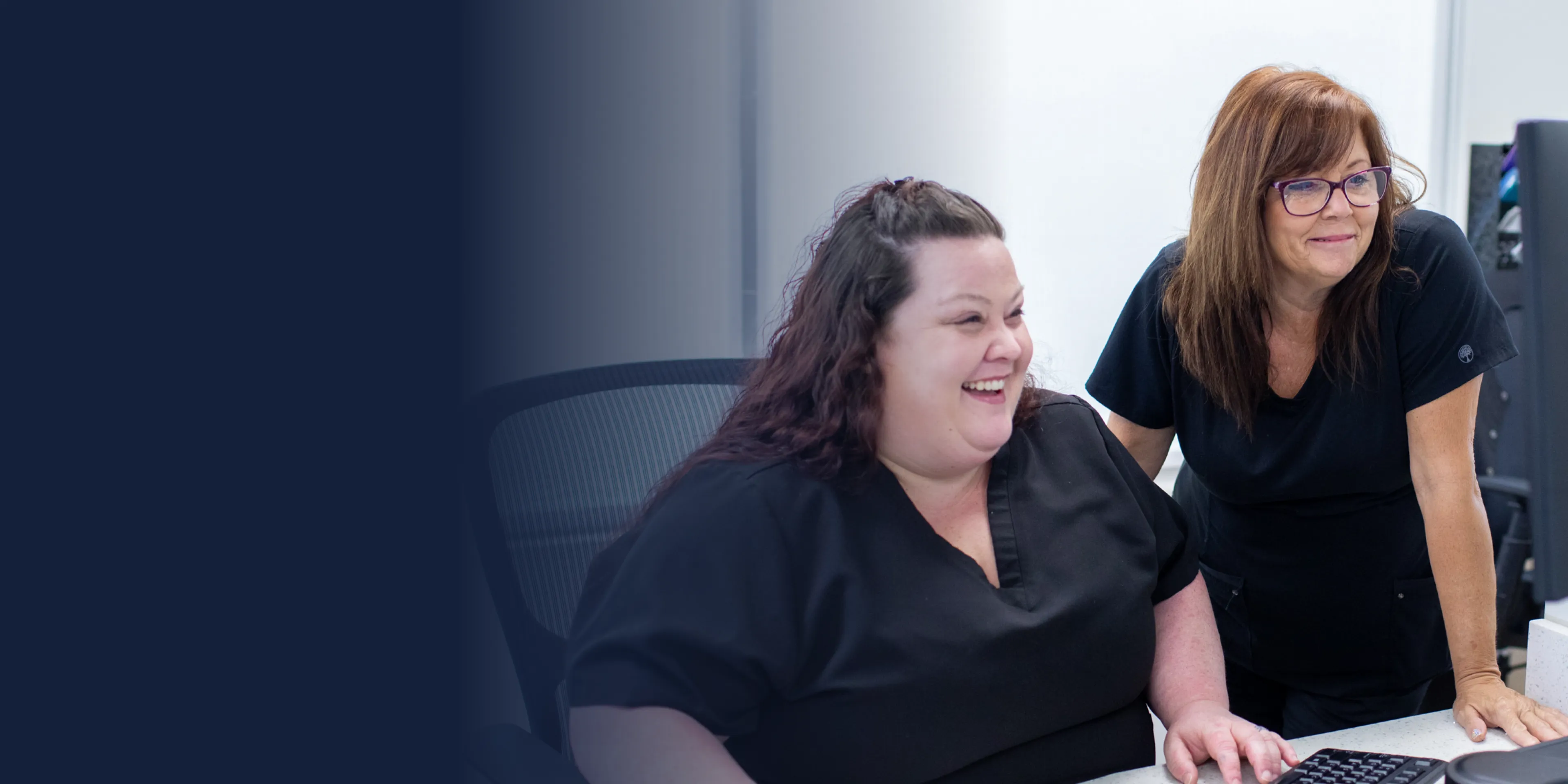 A smiling man in scrubs gives a thumbs-up in an office setting.