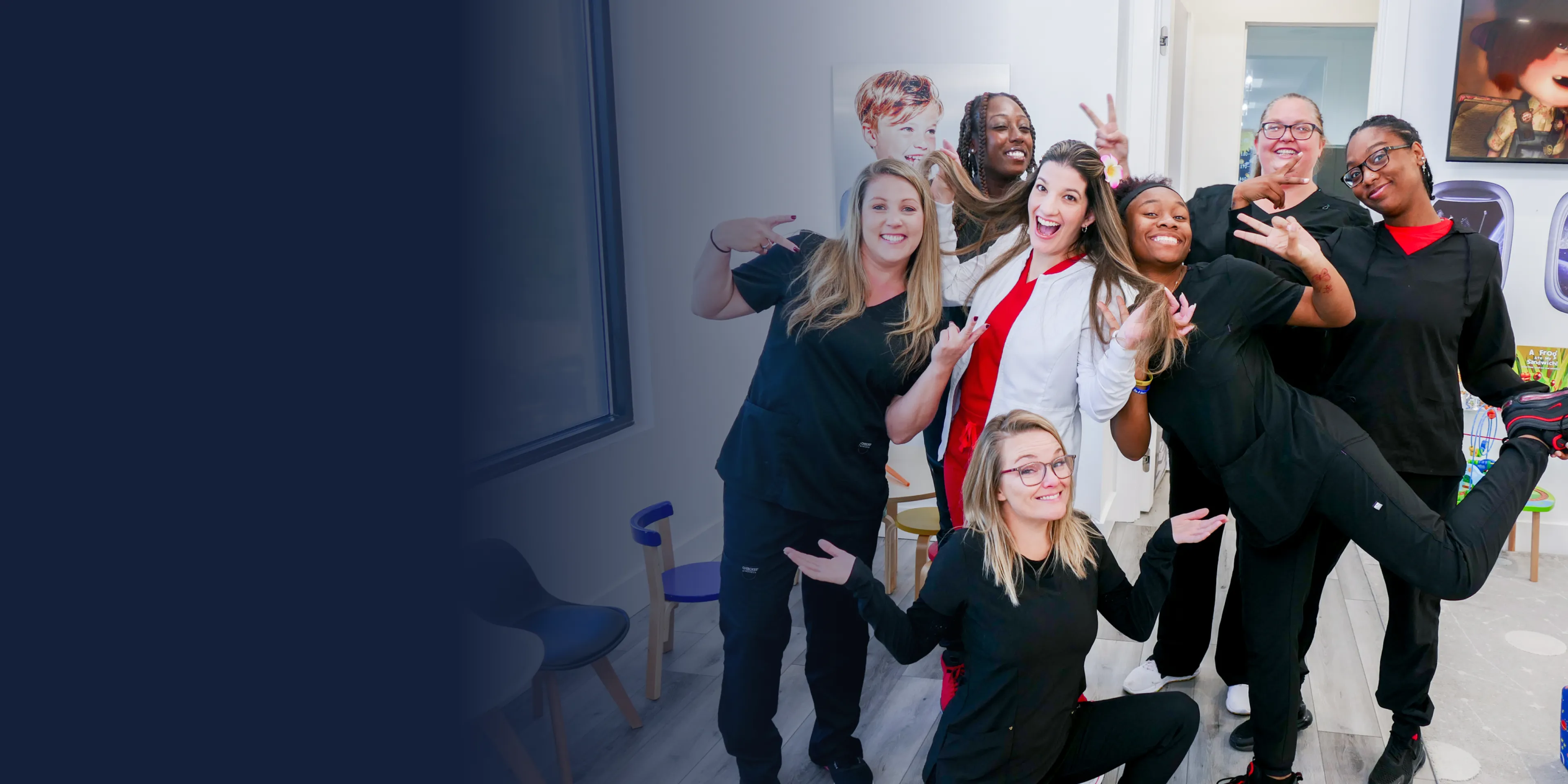 A group of six smiling people, some in scrubs, pose playfully in a dental office.