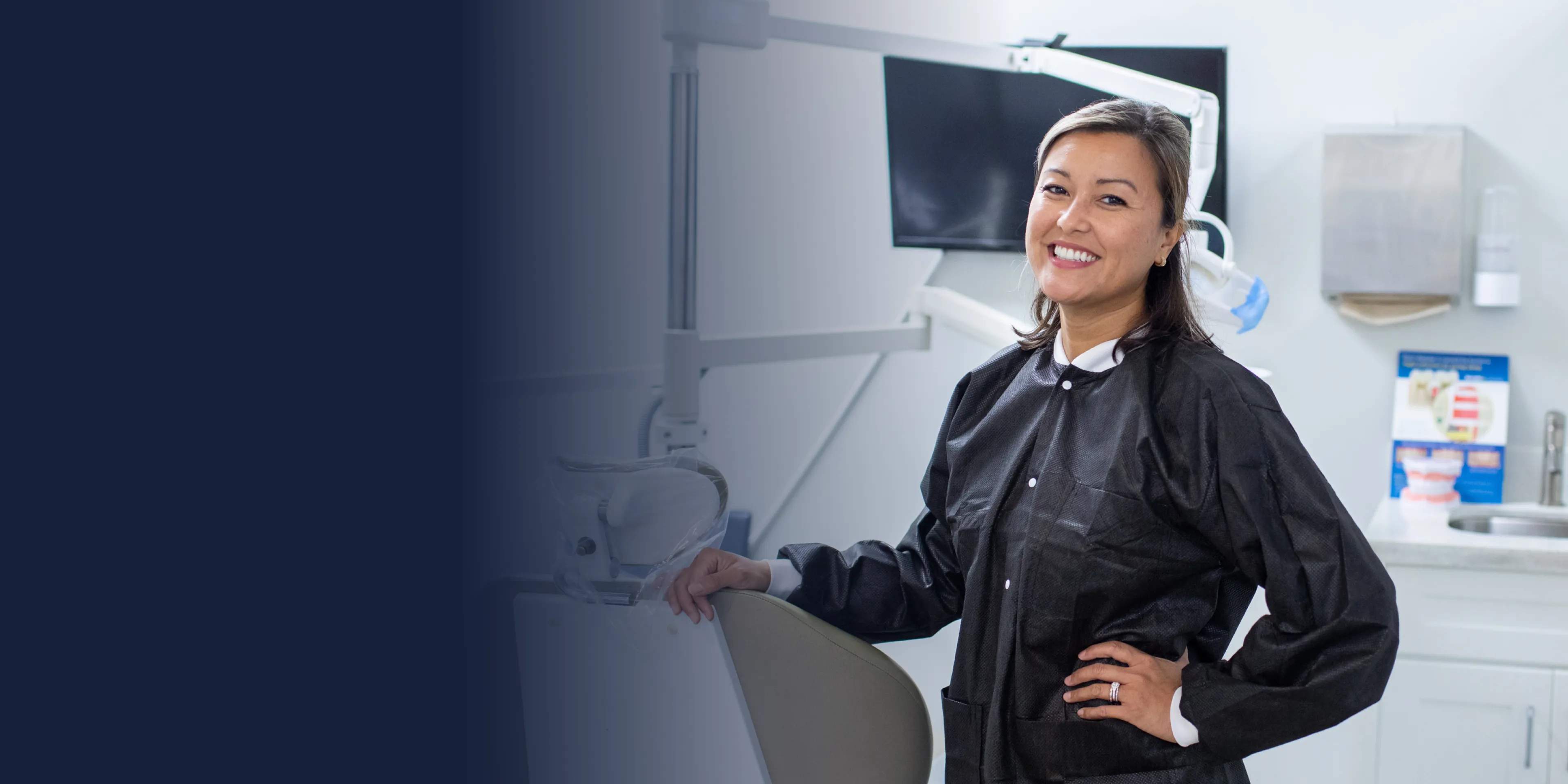 A row of gray chairs is arranged in a waiting room with a TV on the wall.