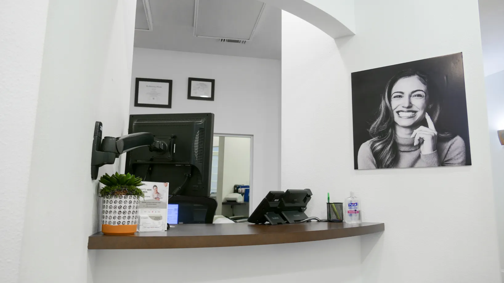 A small reception desk with a computer and a laughing woman's photo on the wall.