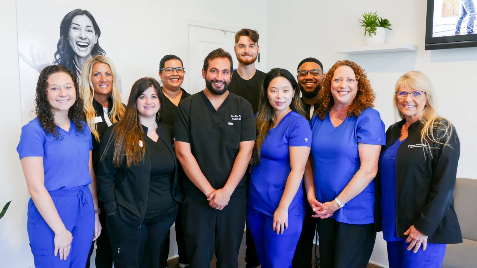 Empty waiting room with gray chairs, a round wooden table, a TV, and large windows.