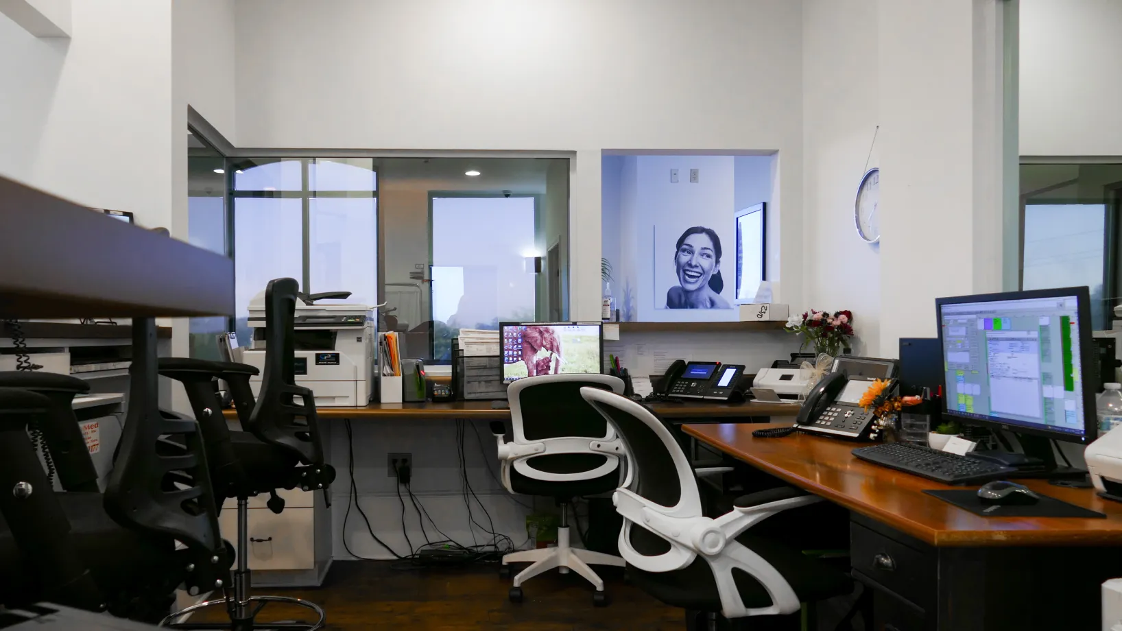 An empty office with multiple desks and chairs, featuring computers and office equipment.