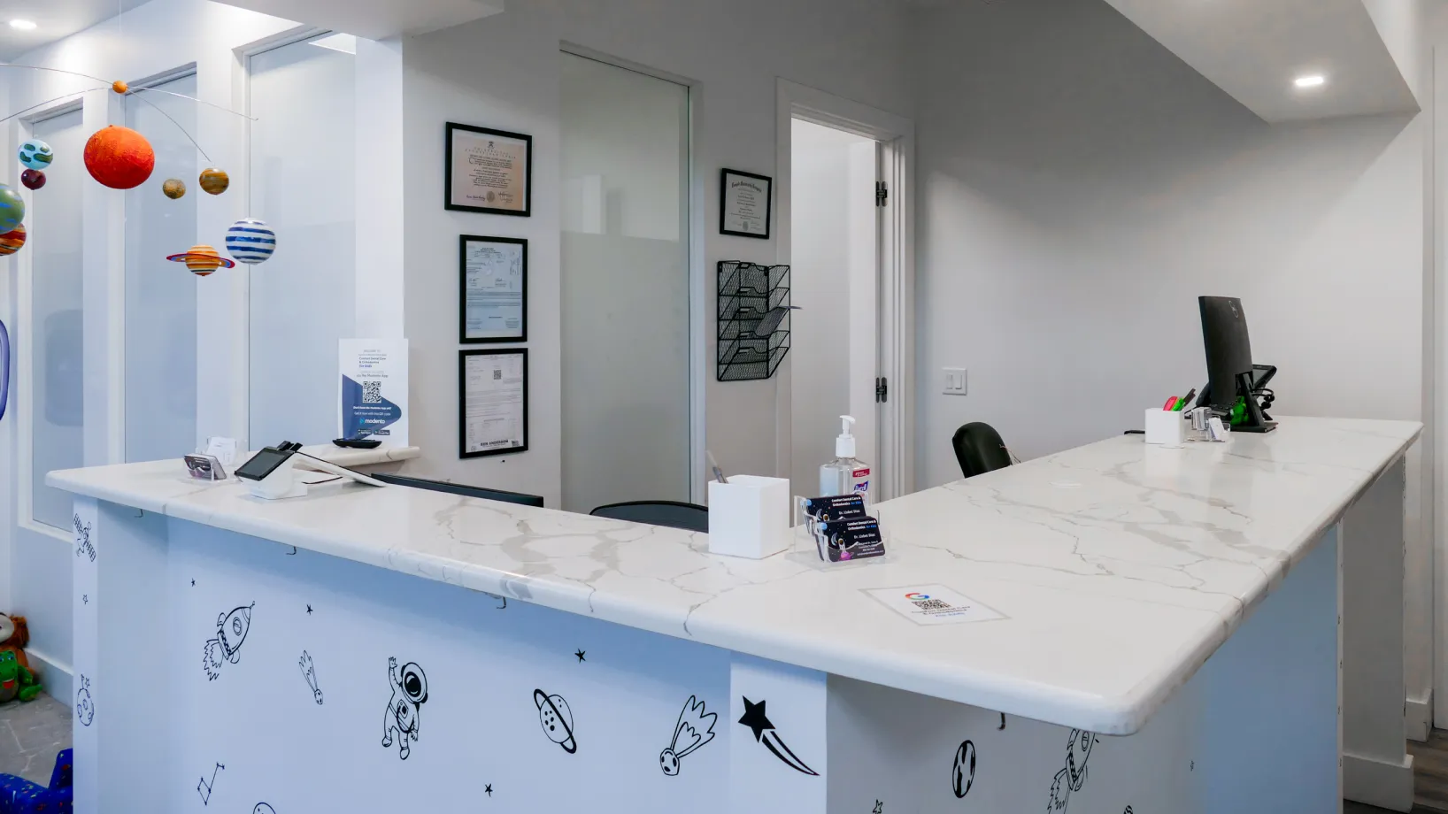 A reception desk with a computer, sanitizer, and decorative space-themed stickers.