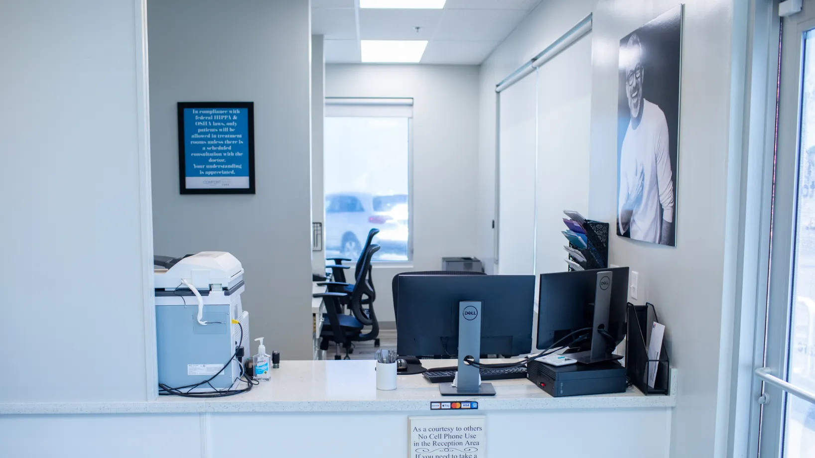 Office reception area with computers, printer, and chairs visible. Portrait hangs on the wall.