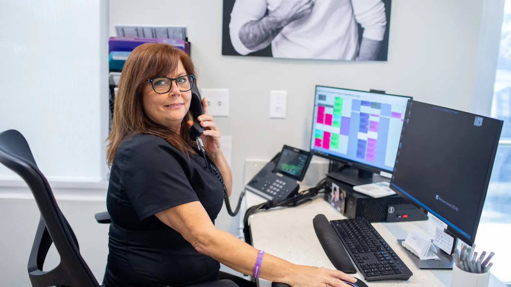 A woman in an office talks on the phone while looking at computer screens.