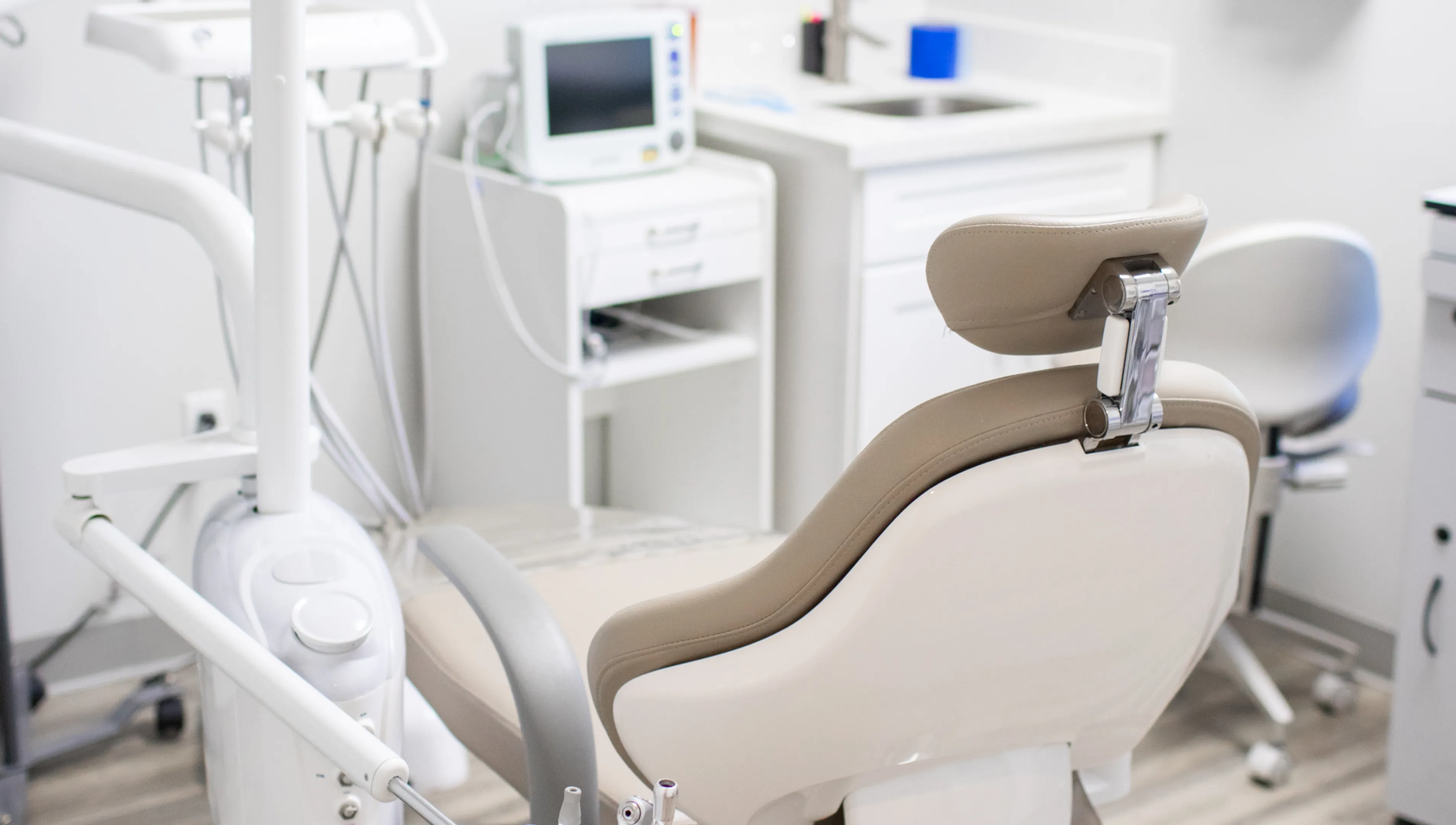 An empty dental chair in a clean, modern dentist’s office with equipment nearby.