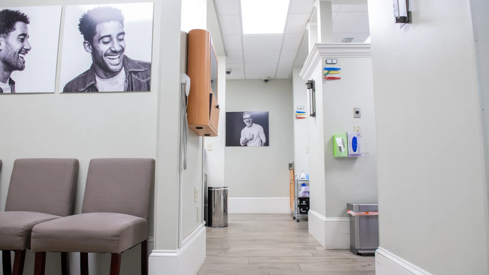A dentist's waiting room with chairs, a waste bin, and a portrait on the wall.