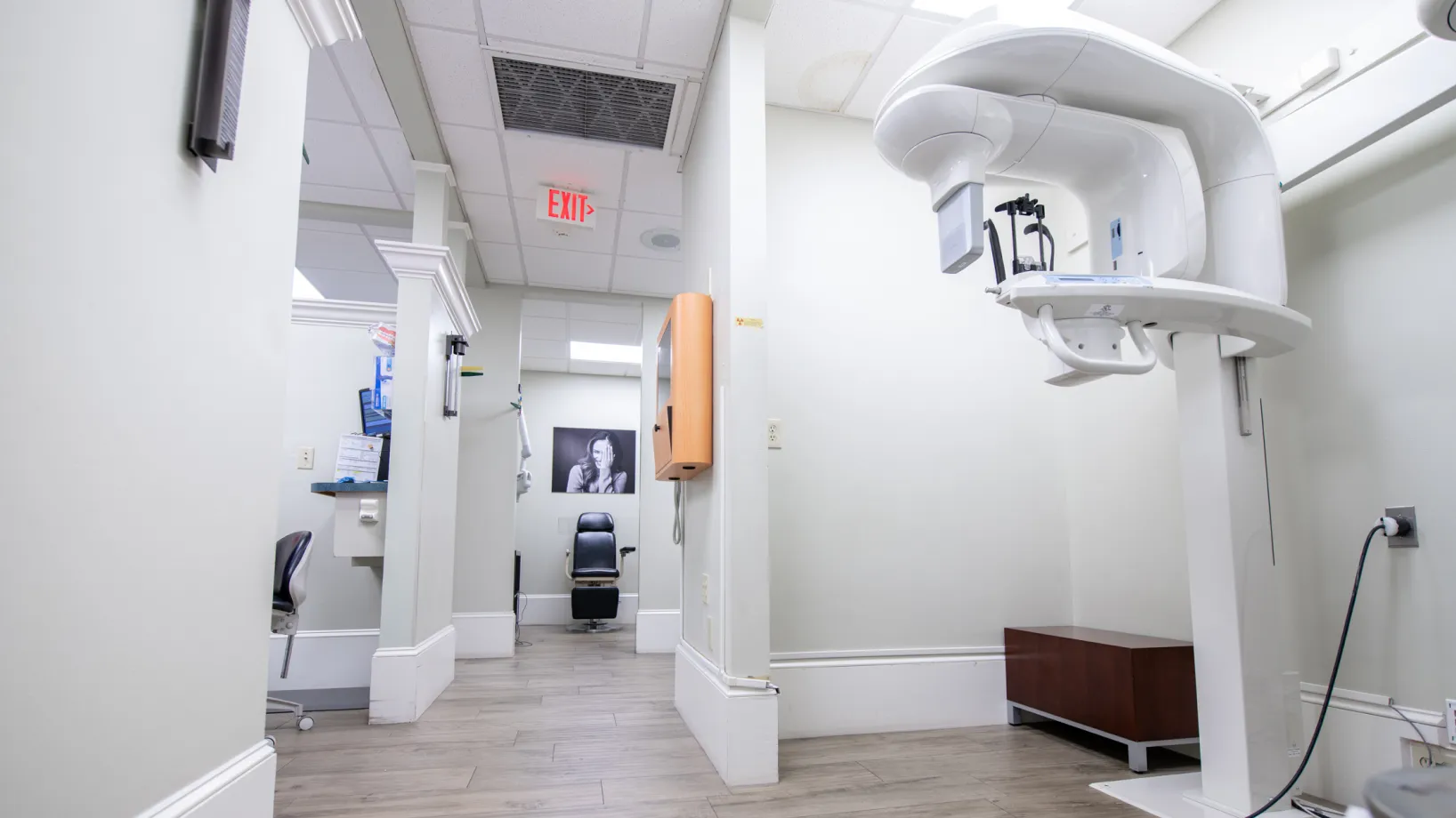 A dental office hallway with an X-ray machine and an empty chair in the background.