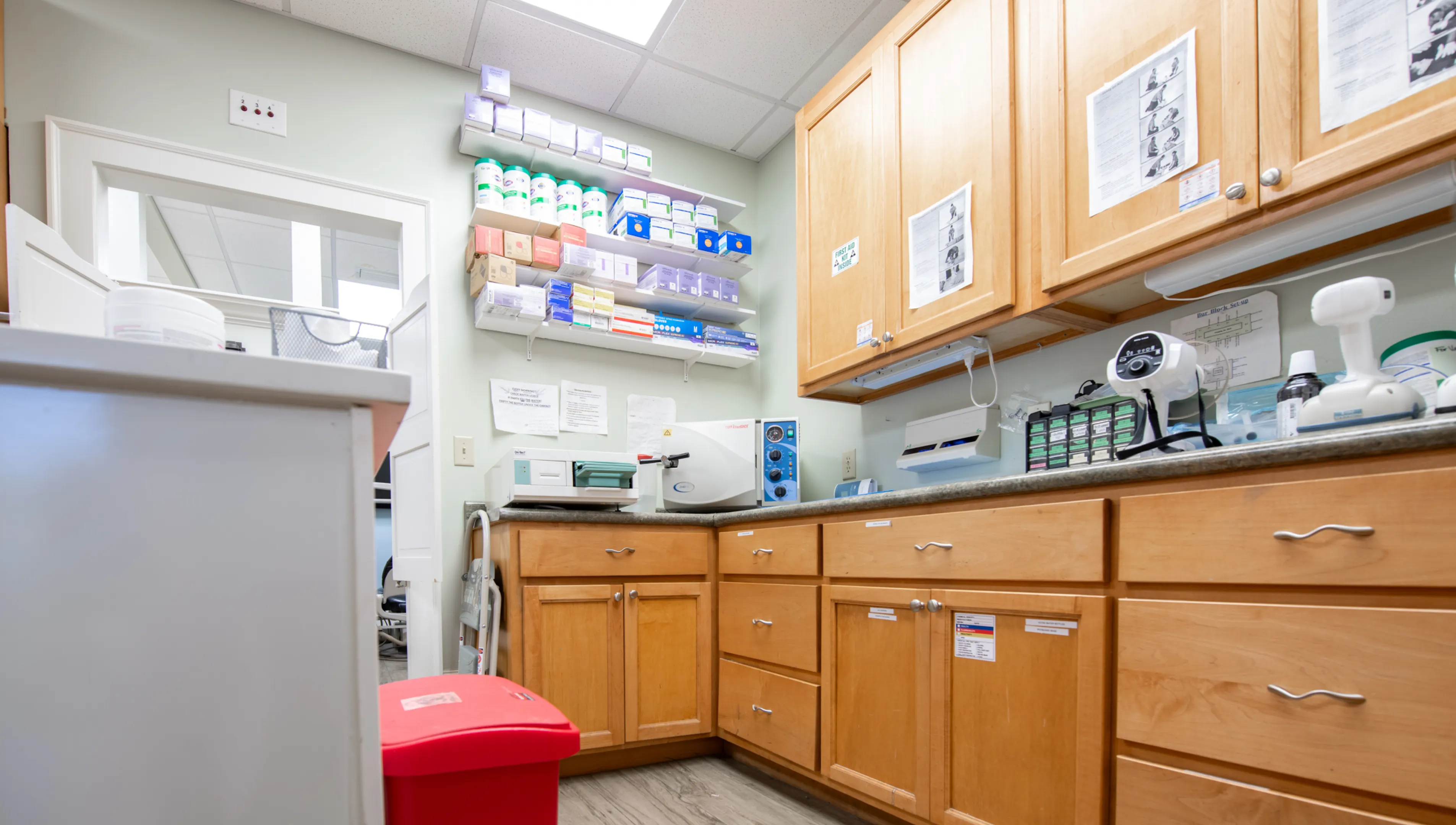 A medical lab room with wooden cabinets, countertop equipment, and neatly organized supplies on shelves.