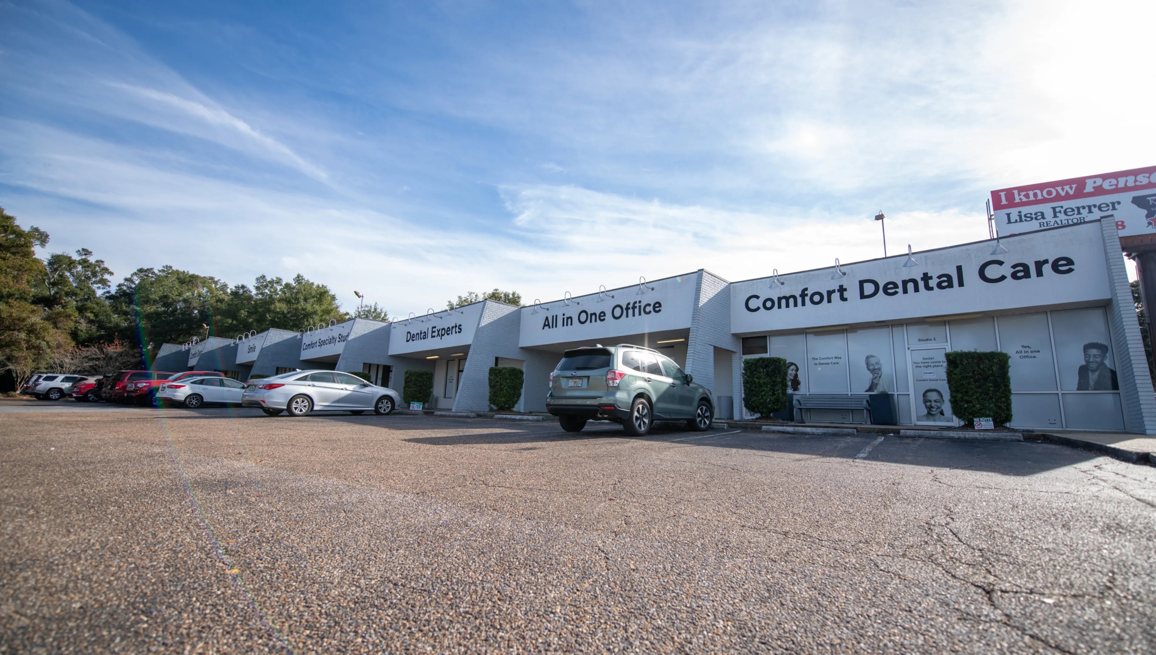 A row of dental offices with parked cars in front and a clear sky above.