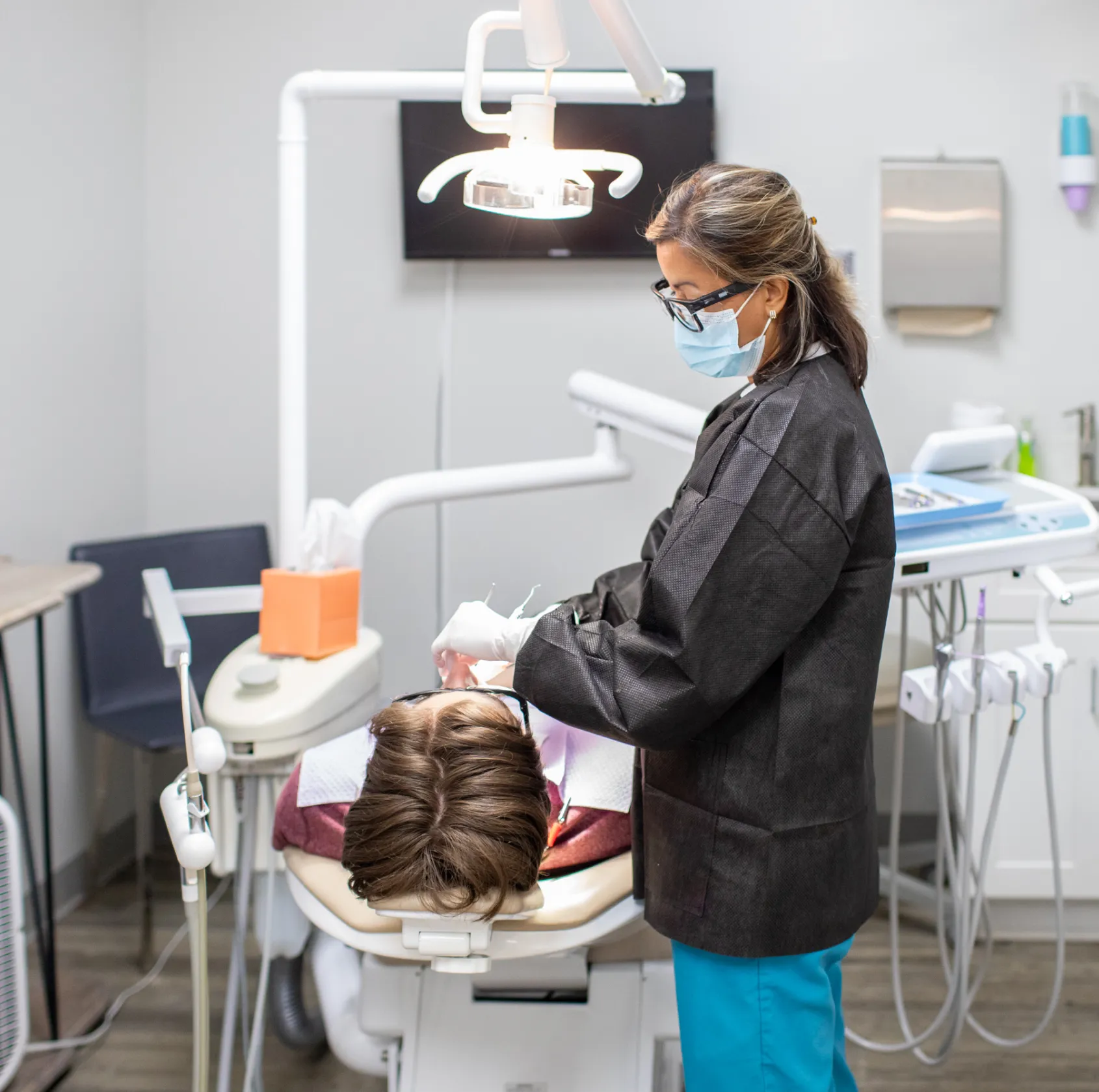 A woman with short gray hair smiles in a dental chair while a dentist stands behind her.